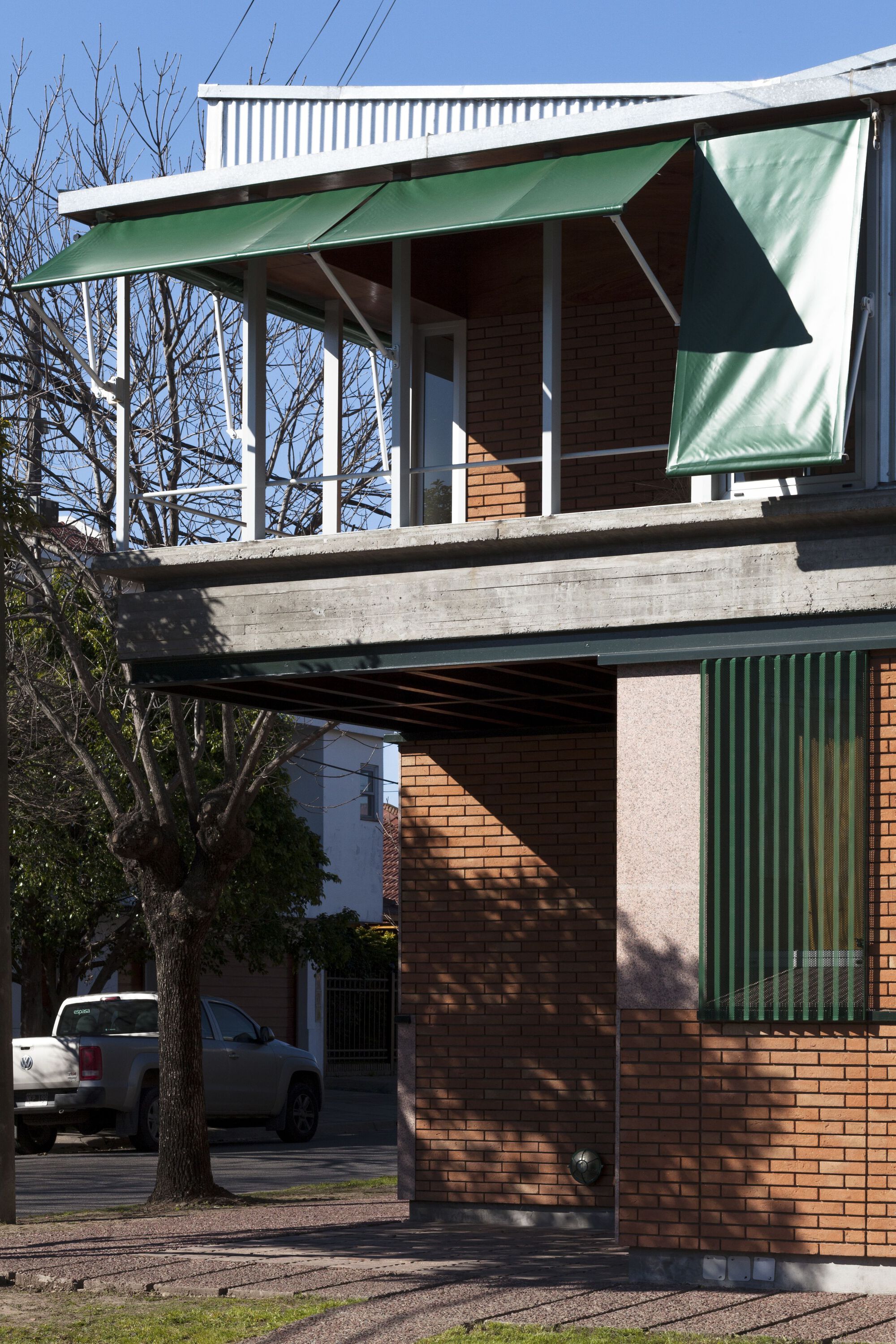 Corner view showing cantilevered concrete slab supporting the upper pavilion with white columns and hinged green awnings