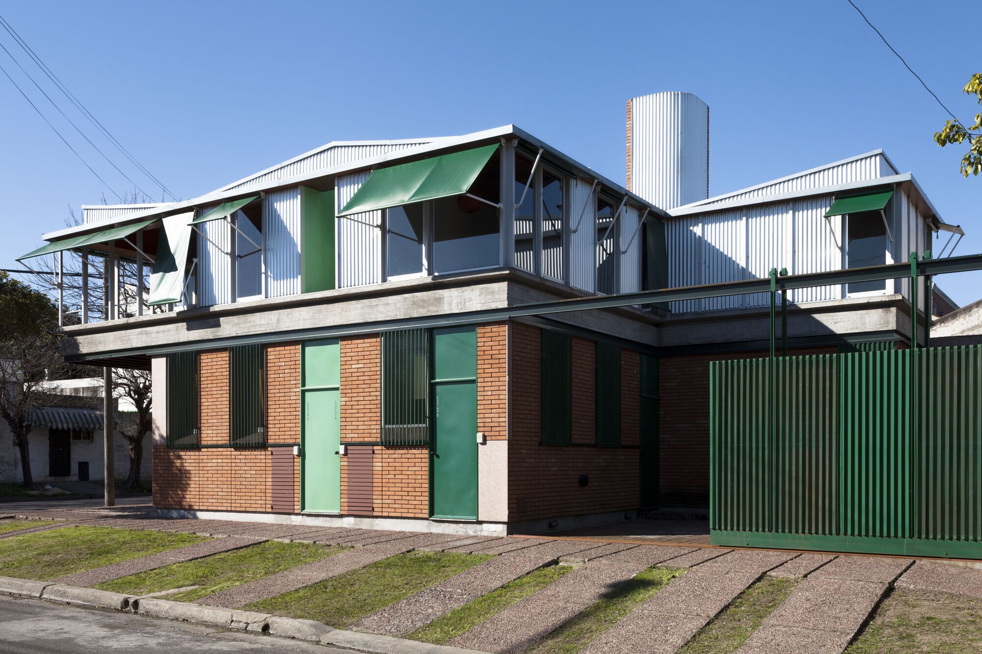 Full facade view showing brick base with green shutters below white corrugated metal upper level and central water tower