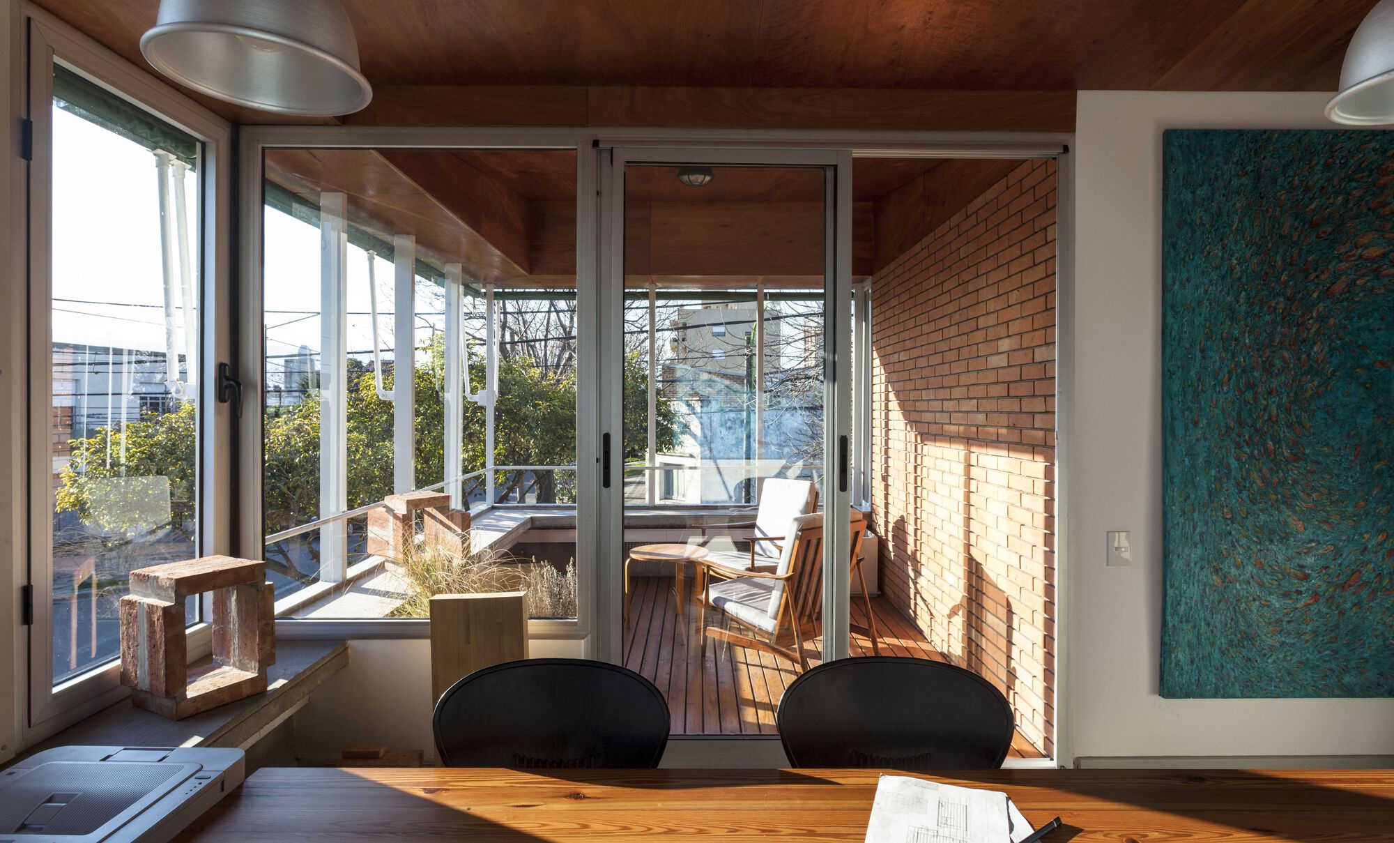Interior dining space with timber ceiling and glazed doors opening to timber deck terrace with planted boxes
