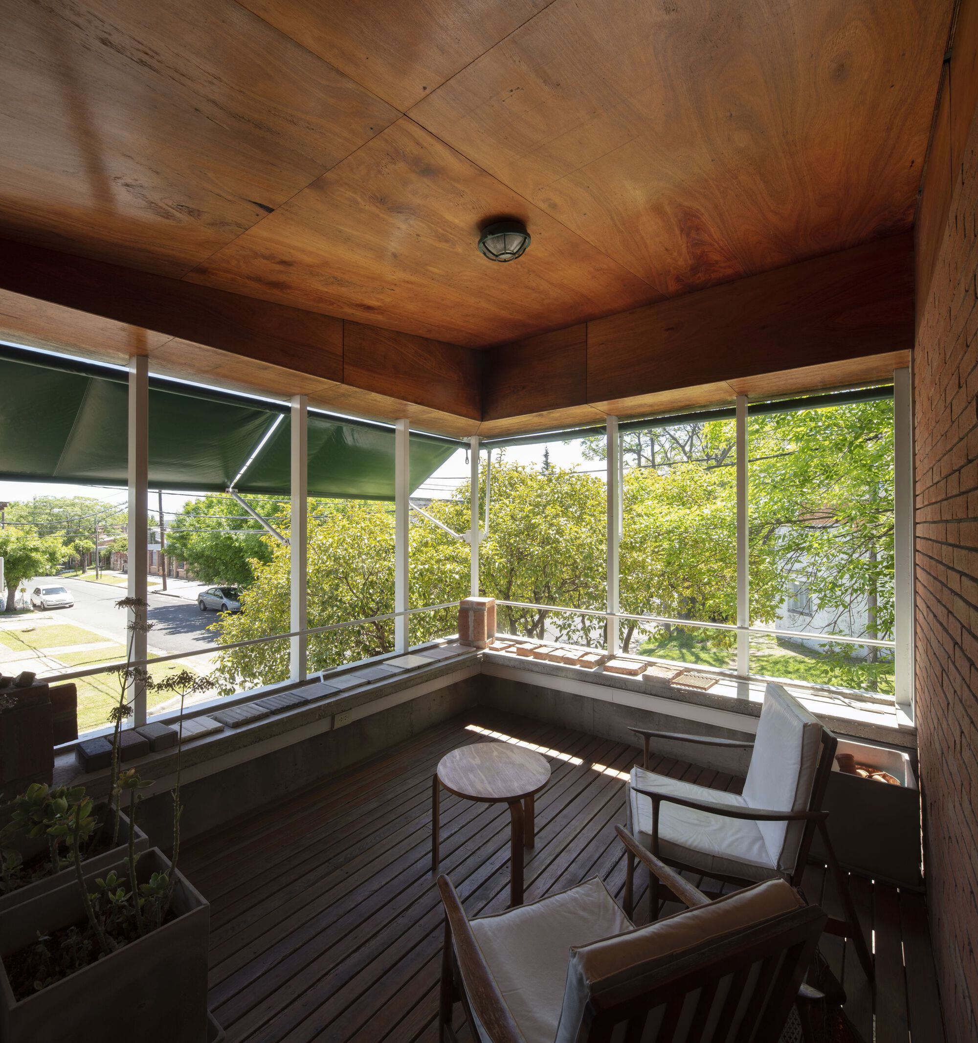 Corner window seat with plywood ceiling and walls framing views of green street trees in afternoon light