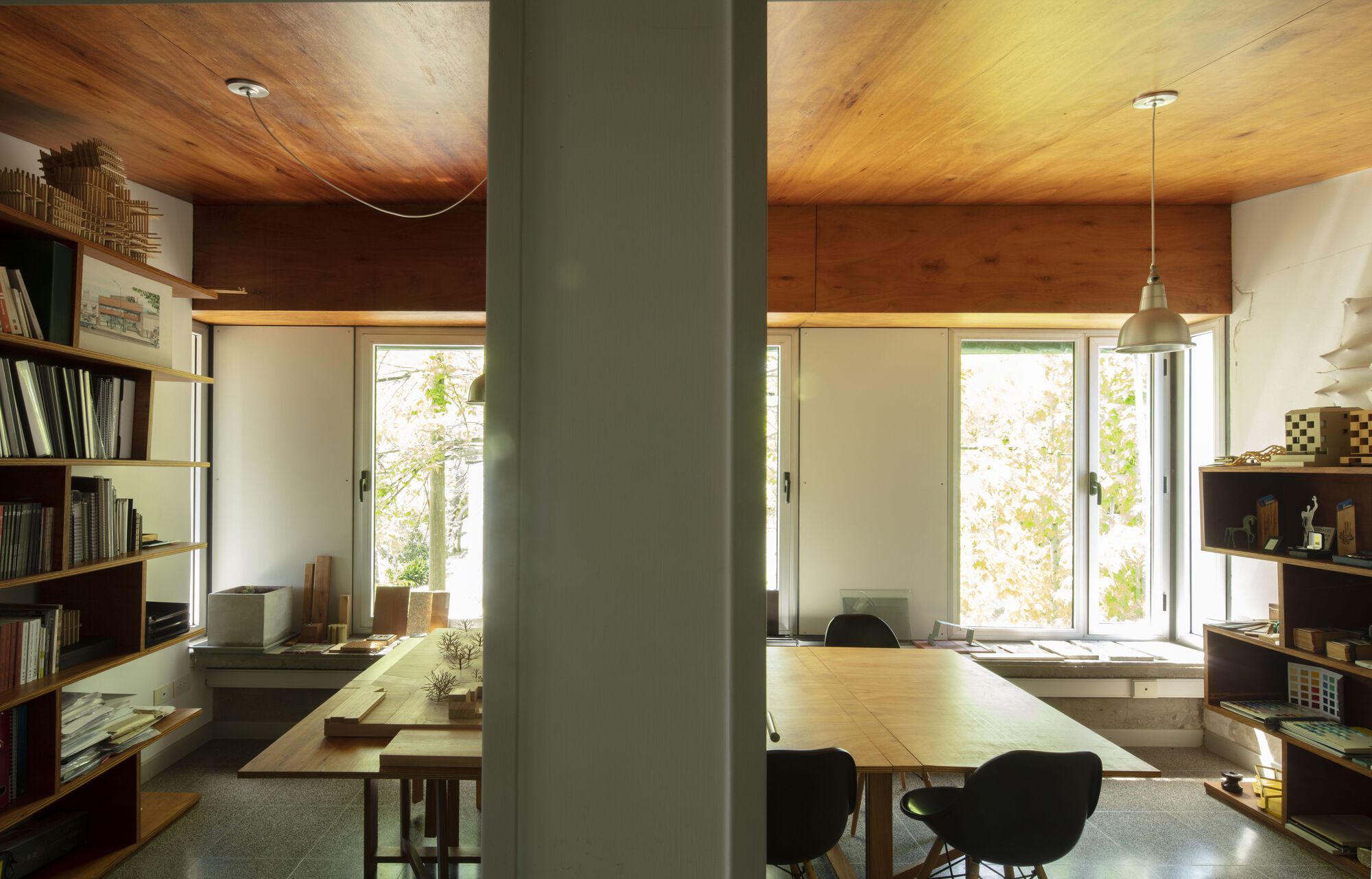 View through grey column into workspace with timber ceiling and open shelving along walls