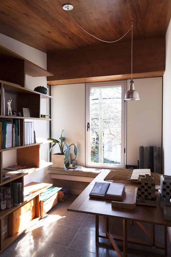 Work desk beneath glazed door with afternoon sun casting shadows across terrazzo floor