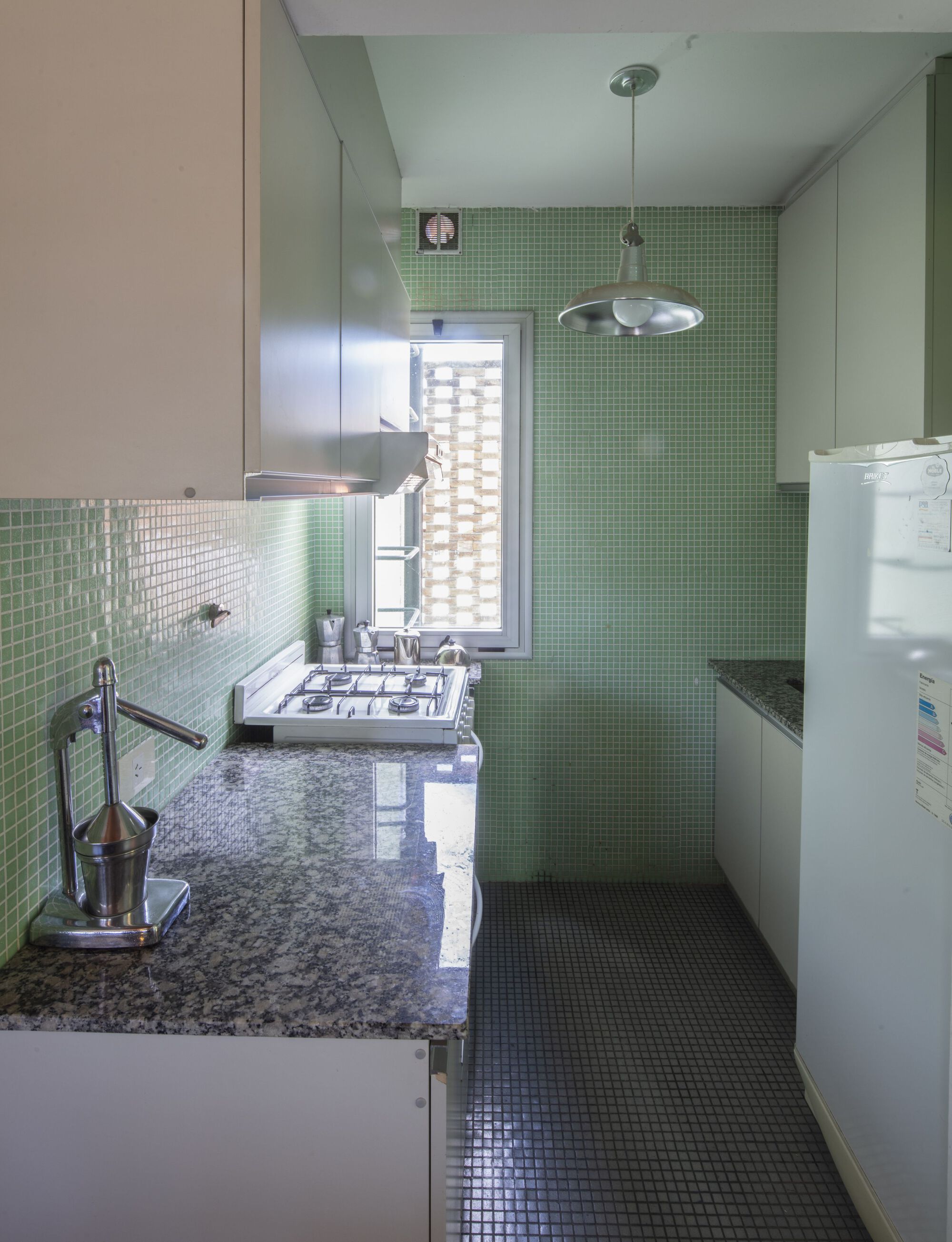 Compact kitchen with green mosaic tile walls and granite countertop under pendant light