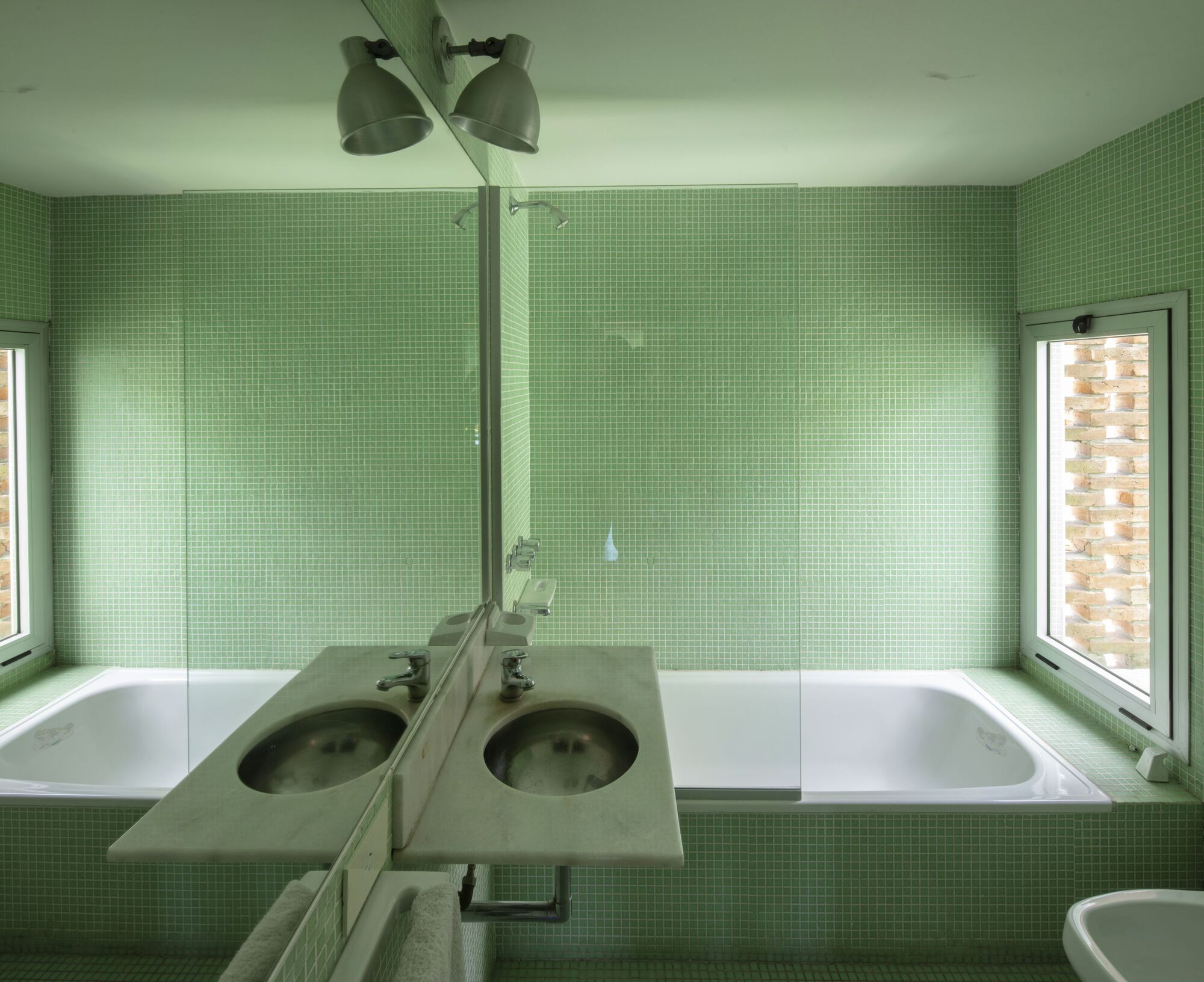 Bathroom with green mosaic tile walls, recessed tub, and dual sinks under ceiling-mounted fixture