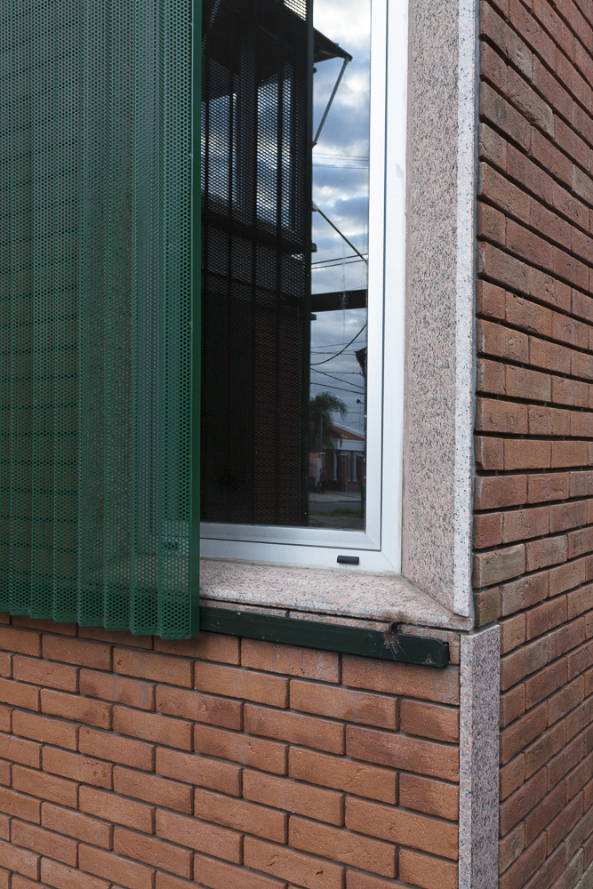 Window corner with green metal screen, granite sill and red brick wall under overcast sky