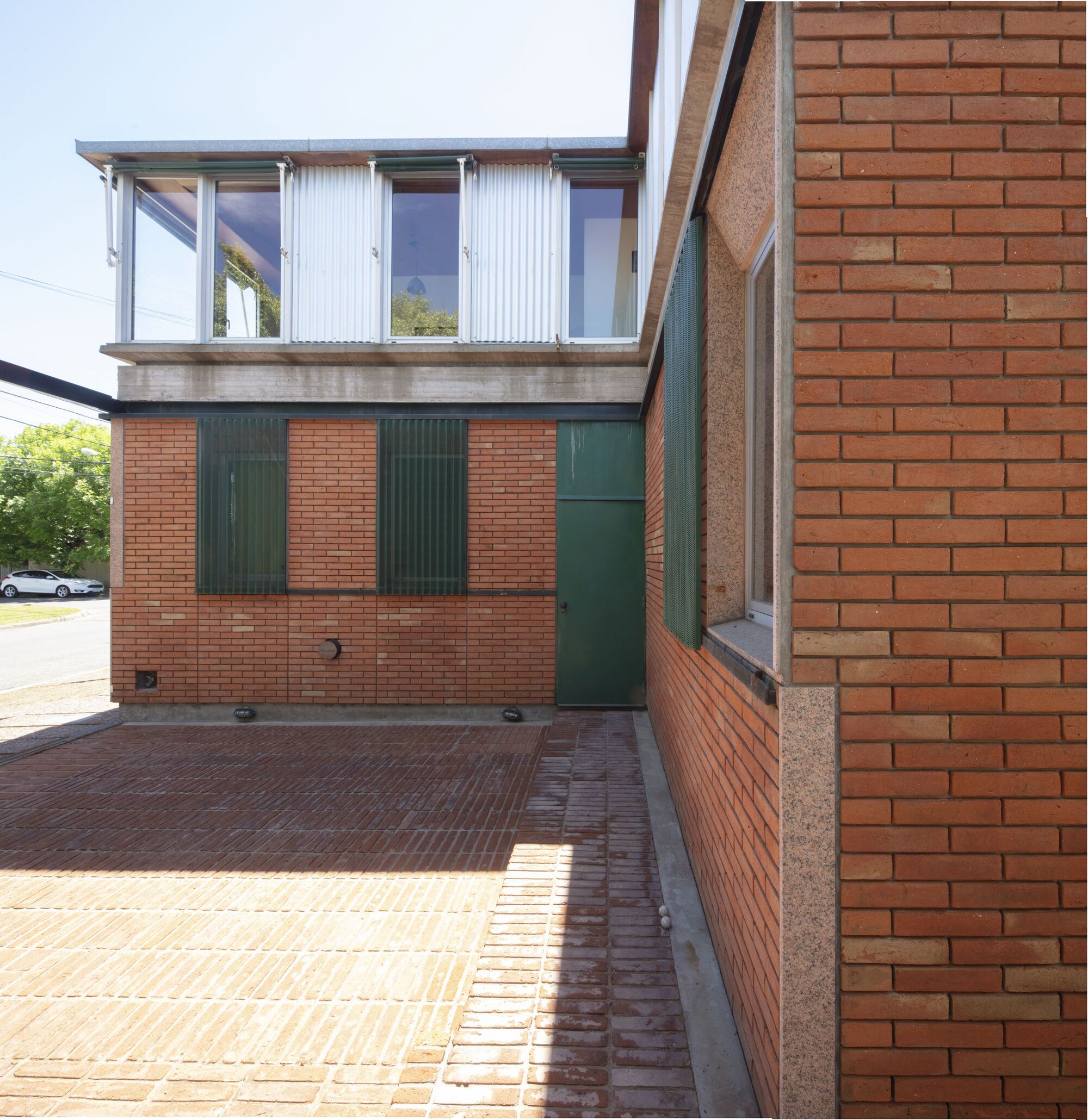 Courtyard with brick paving, red brick walls, green metal shutters and upper corrugated metal volume