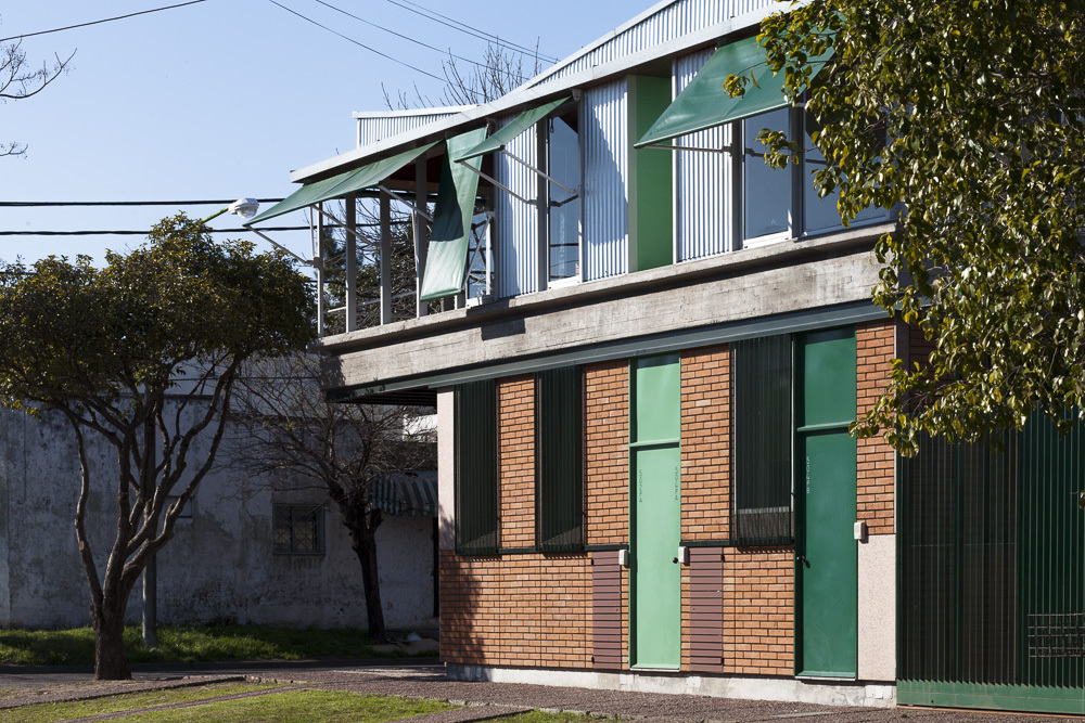 Facade showing red brick base with green metal doors and corrugated metal upper level beside bare tree