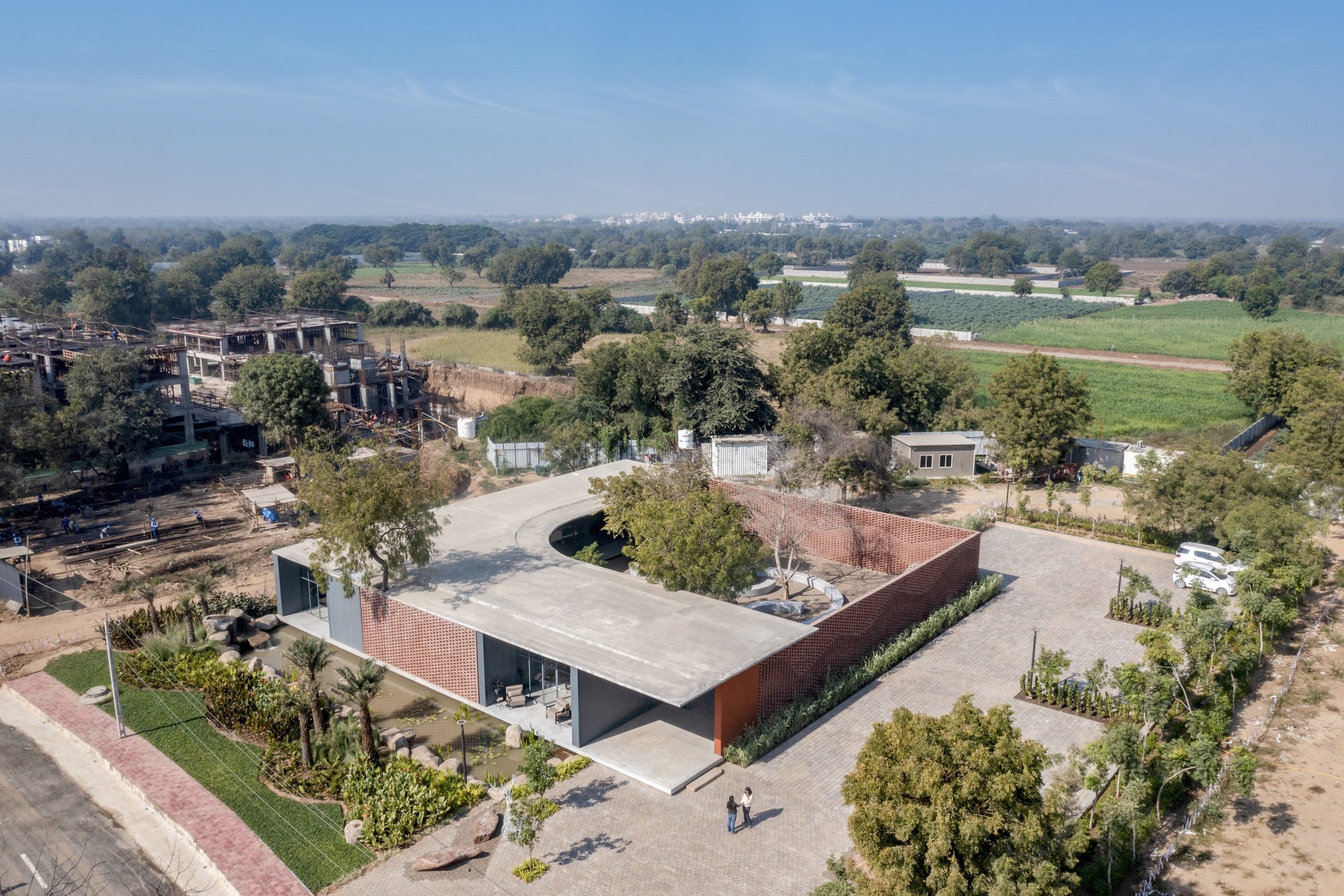 Aerial view of the low-slung concrete roof with perforated brick volume set among agricultural fields and trees