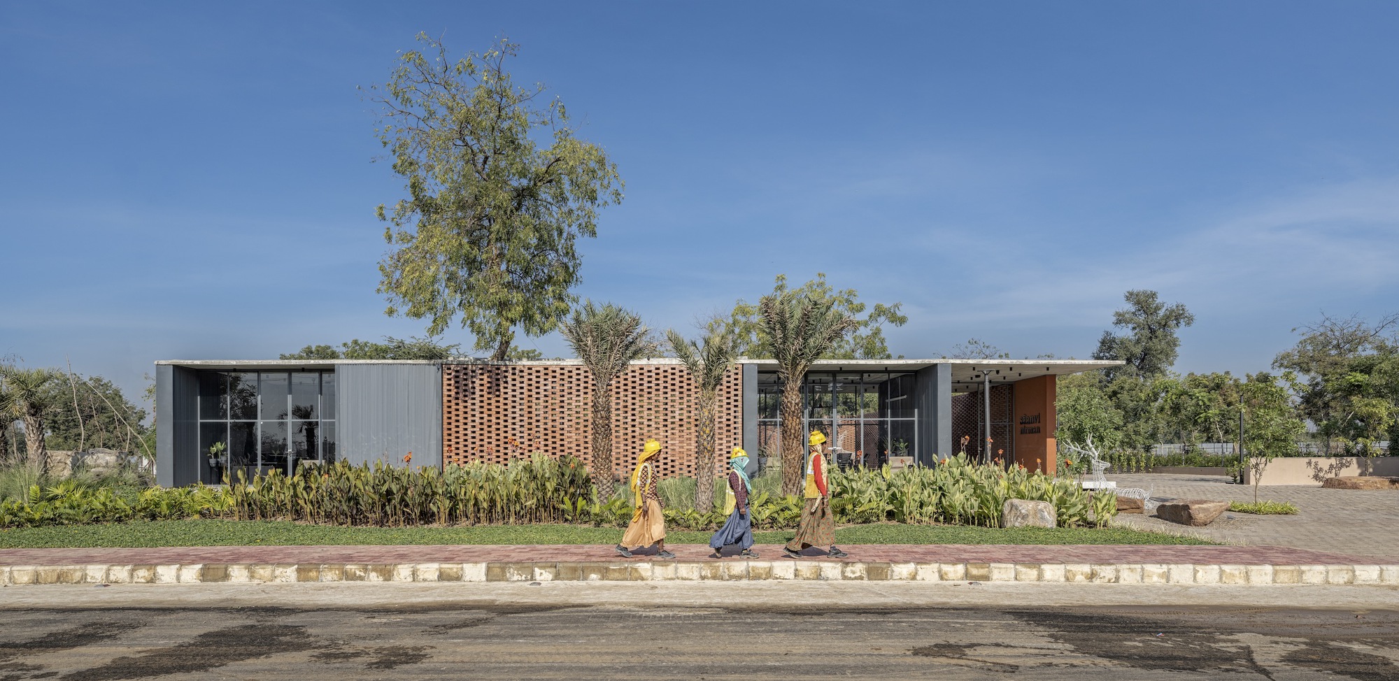 Street view of the perforated brick screen facade with three pedestrians walking along the paved curb