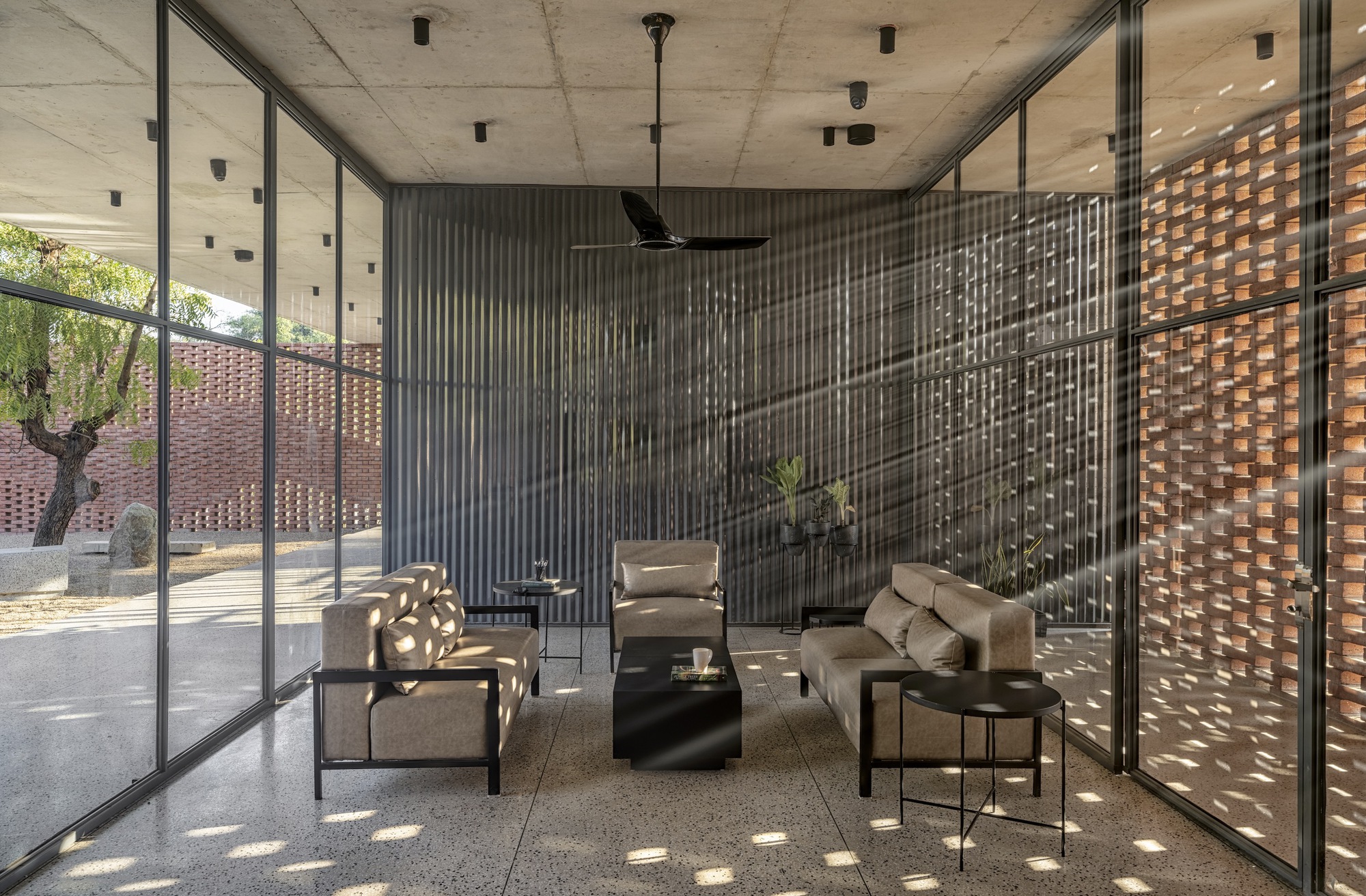 Interior living space with concrete ceiling and corrugated metal screen filtering dappled light from the courtyard