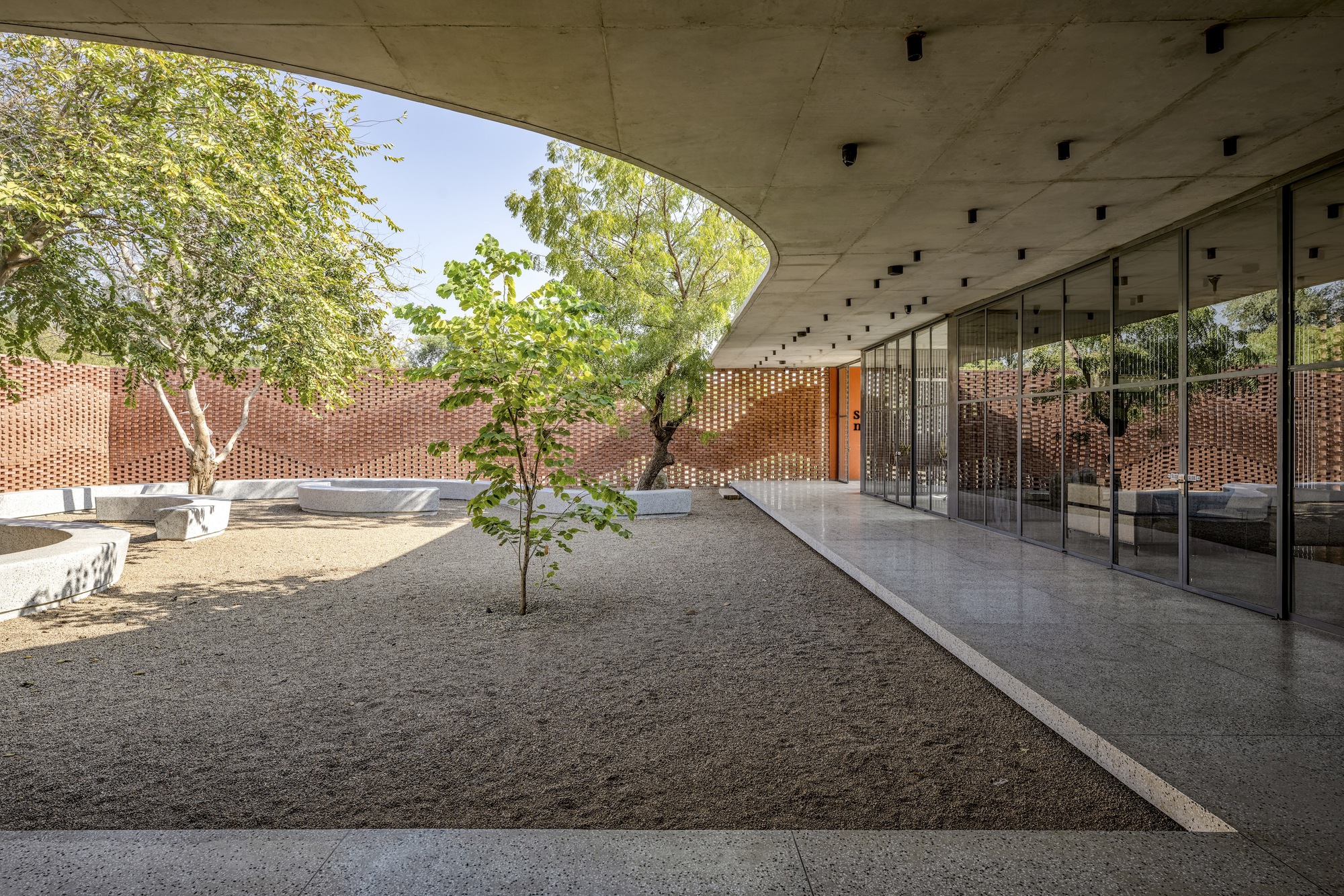 Covered courtyard beneath a curved concrete roof with glazed walls and gravel ground plane