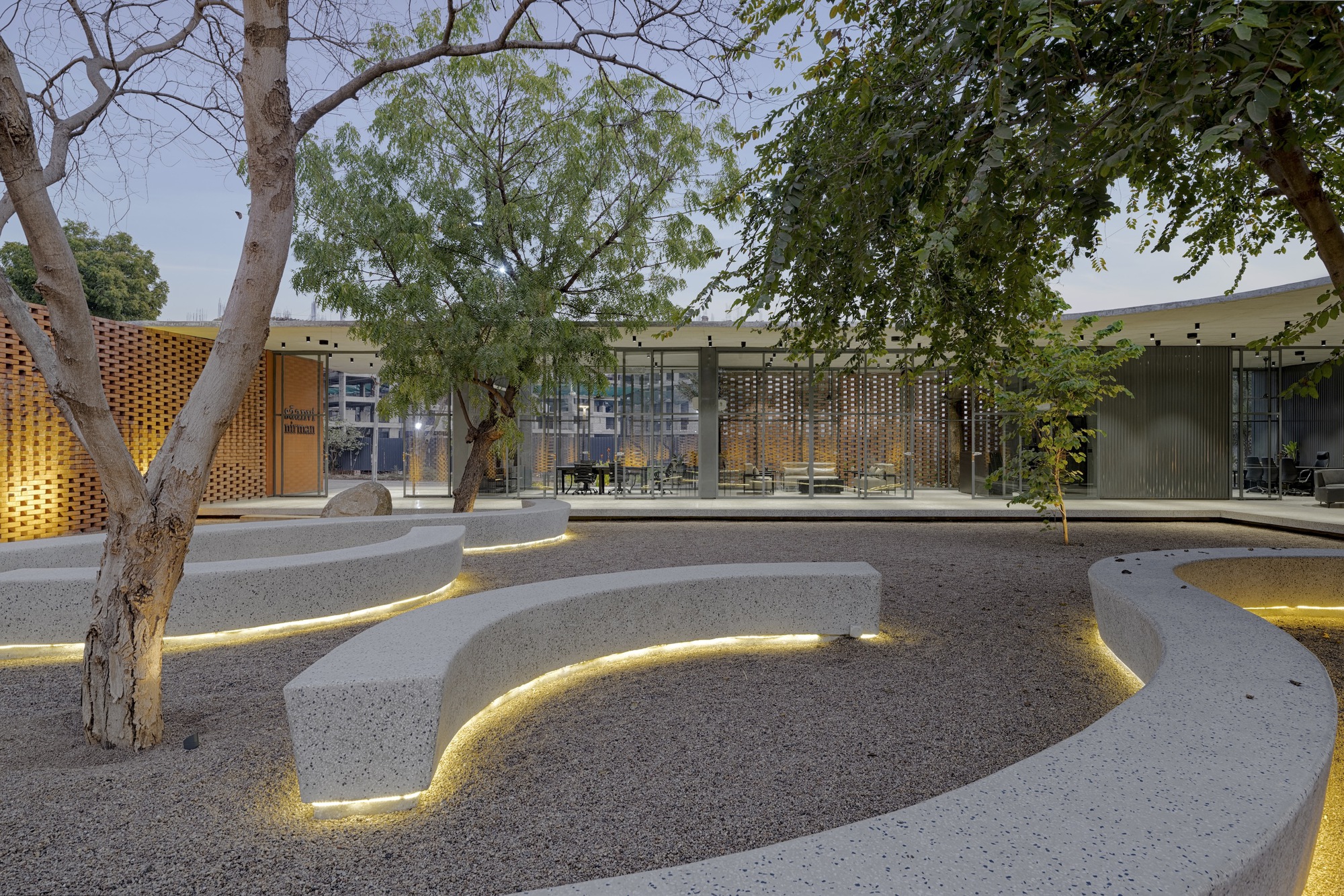 Terraced gravel seating area with integrated strip lighting at dusk beneath mature trees