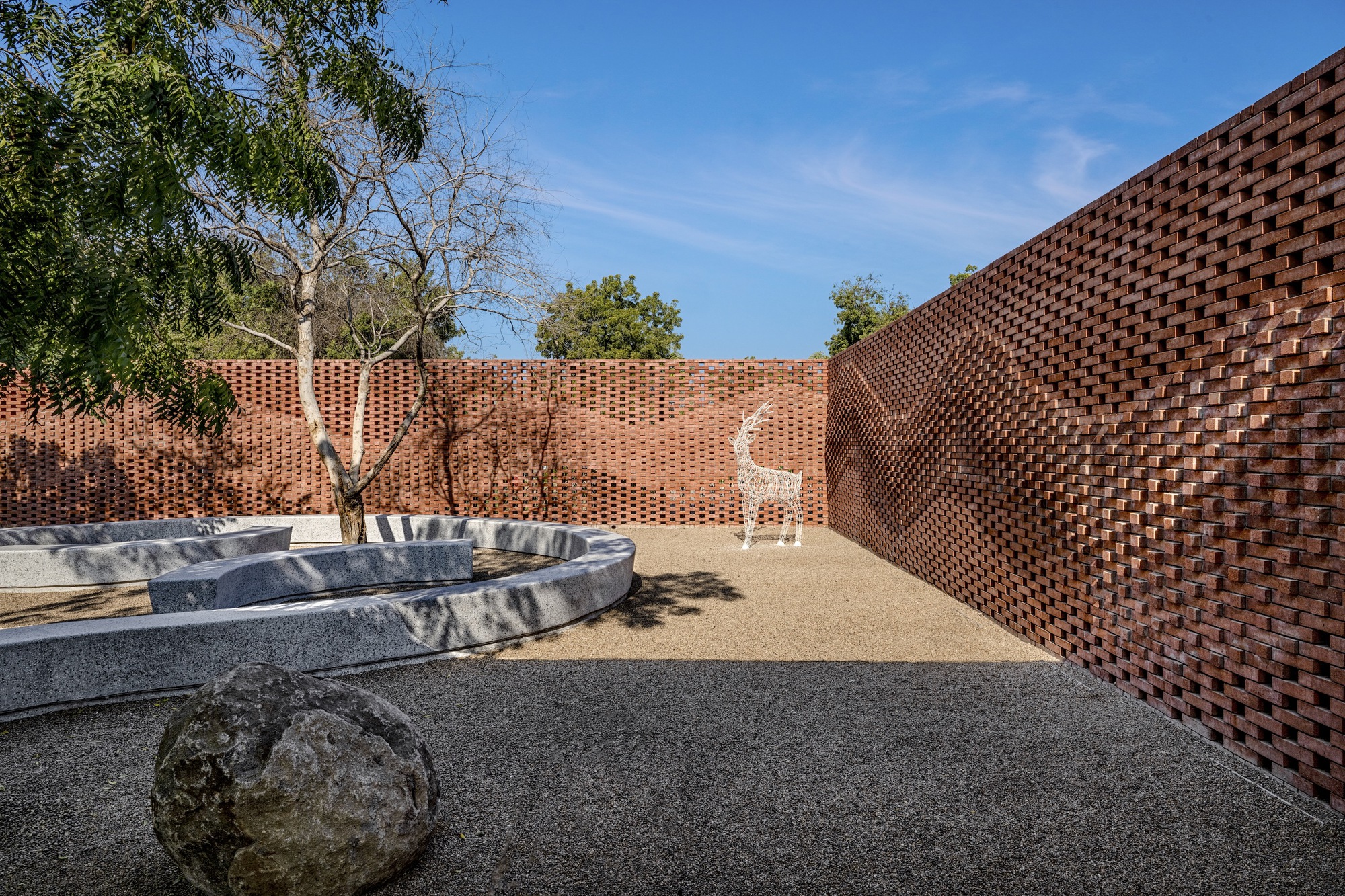 Enclosed courtyard with perforated brick walls surrounding a curved concrete planter and gravel floor