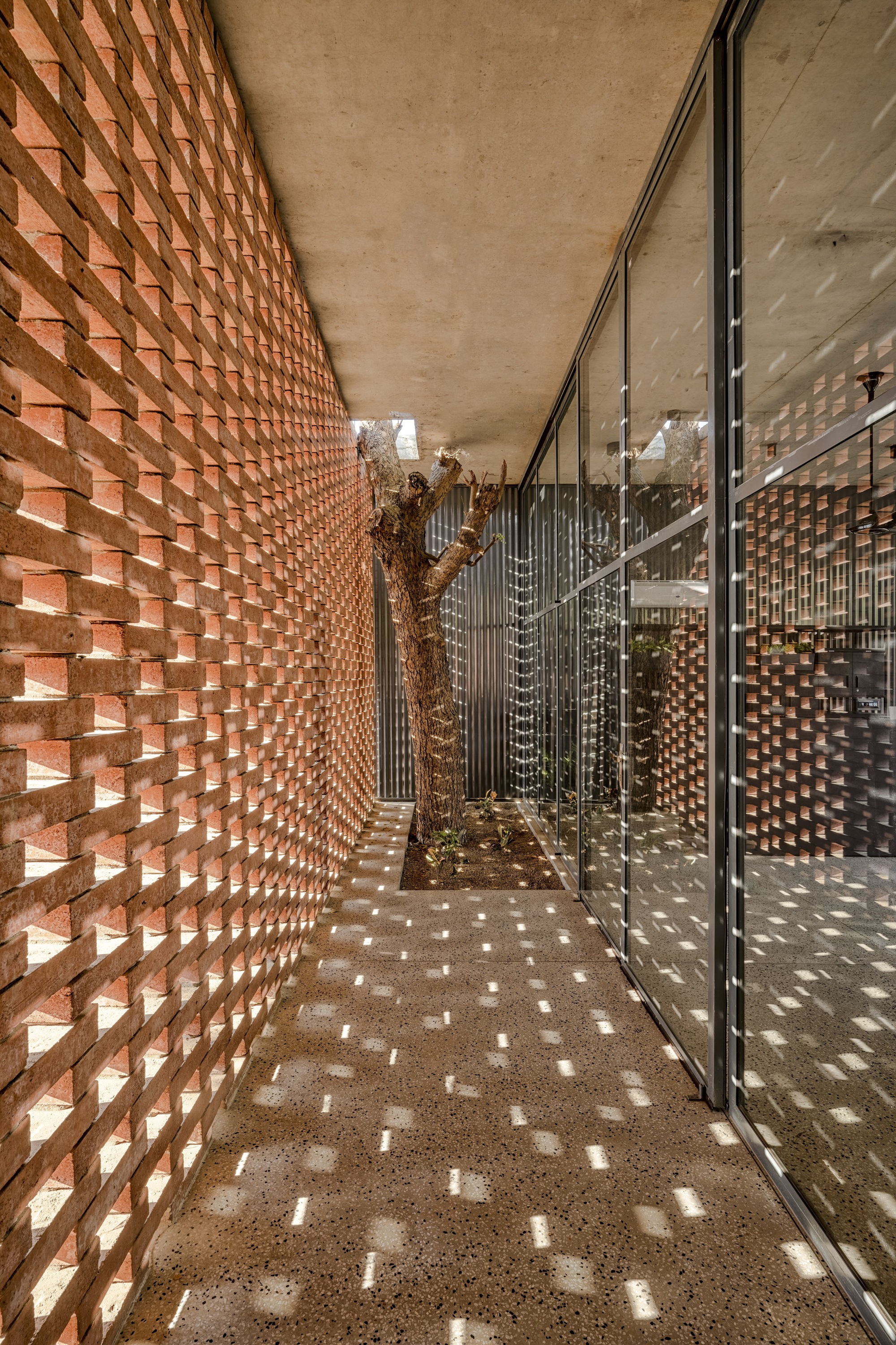 Perforated terracotta brick wall corridor casting dappled sunlight onto polished terrazzo flooring