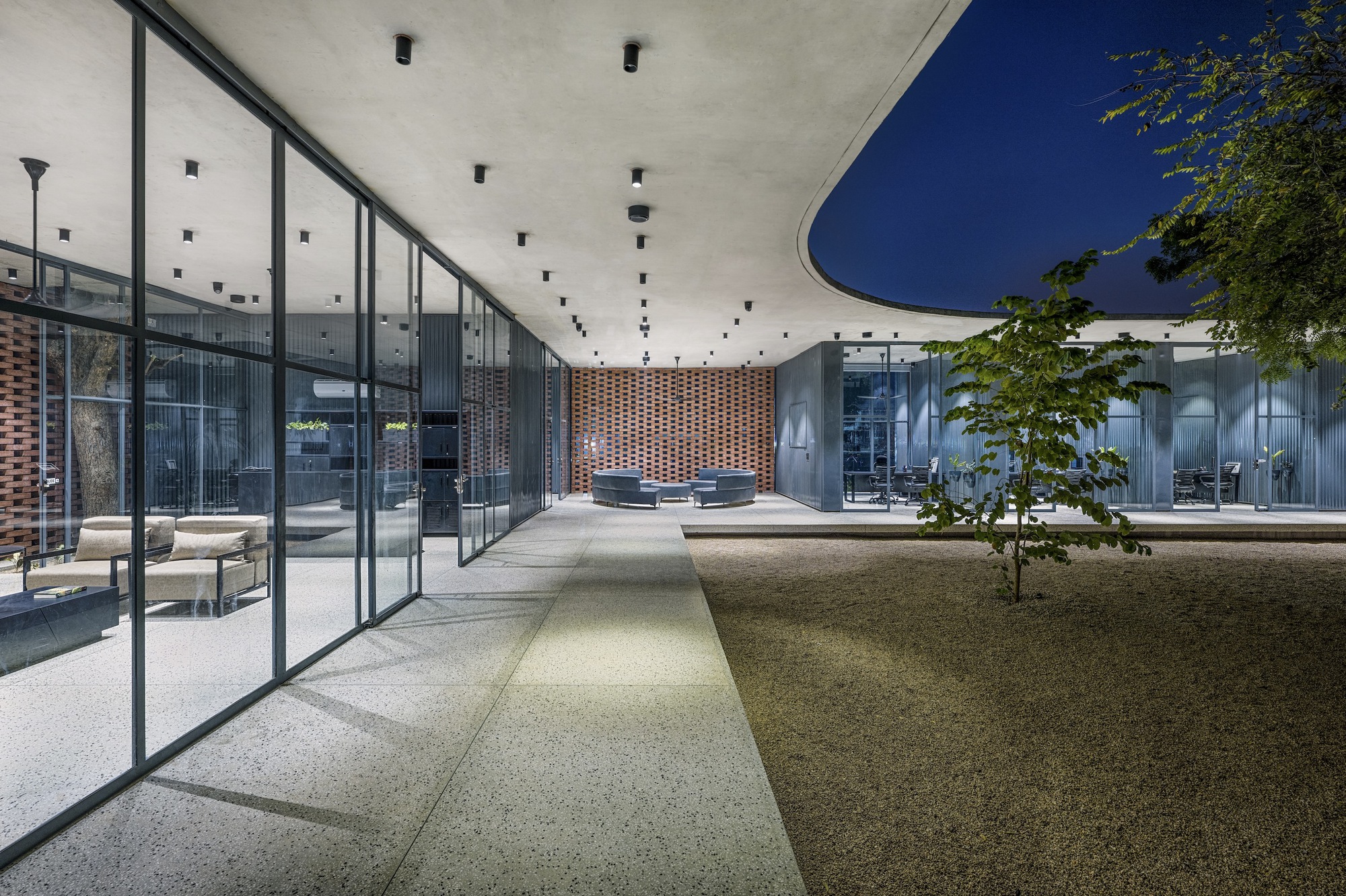 Central courtyard at dusk with gravel paths converging beneath a concrete roof and perforated brick screen wall