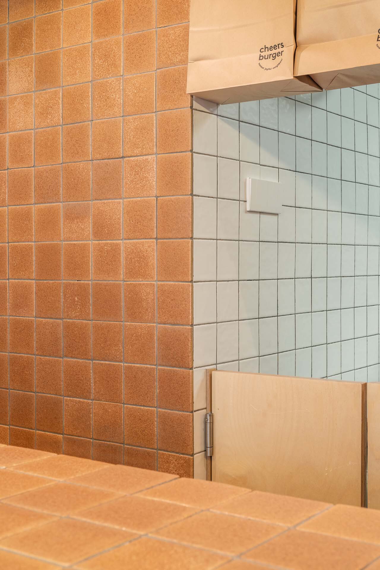 Junction of orange and pale green tiled walls with recessed white paper towel dispenser
