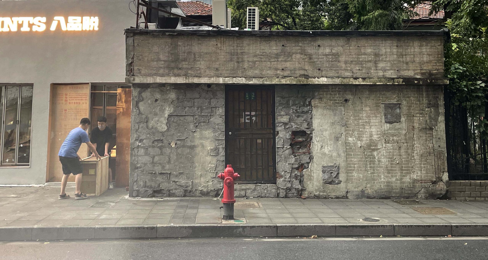 Weathered concrete structure with boarded windows and red fire hydrant on sidewalk