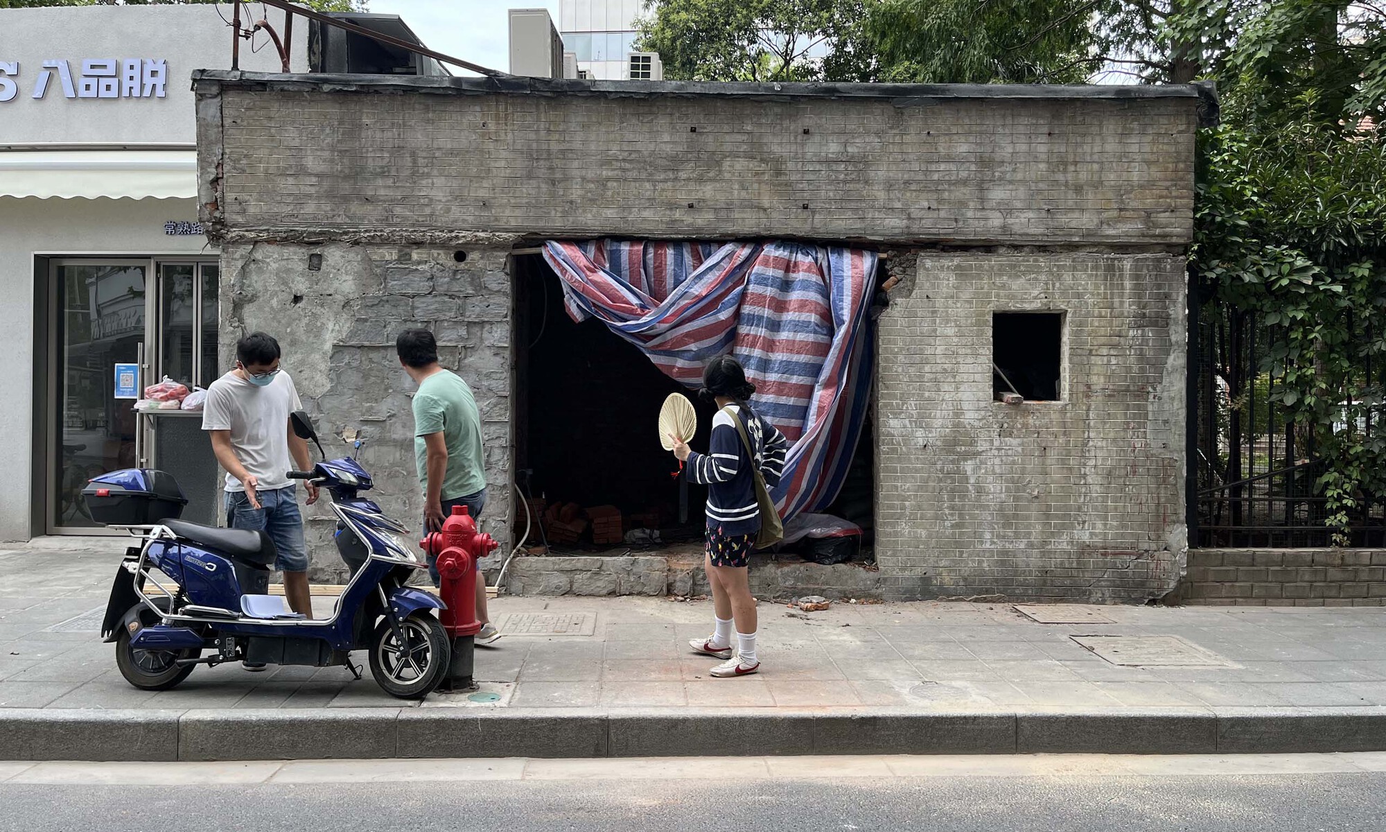 Derelict concrete building with striped curtain covering opening and pedestrians gathering on the street