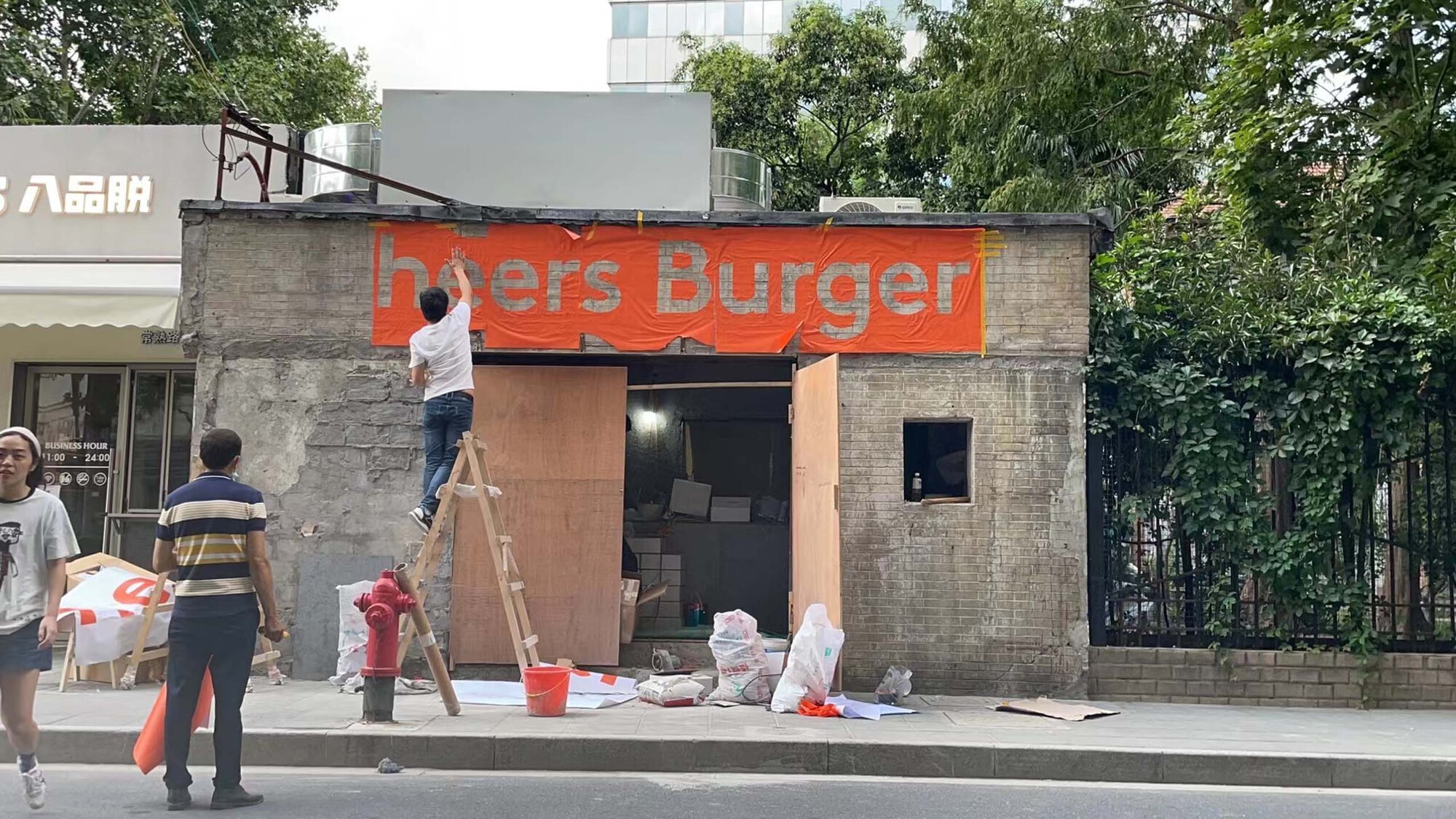 Weathered concrete facade with orange signage being installed by workers on a ladder