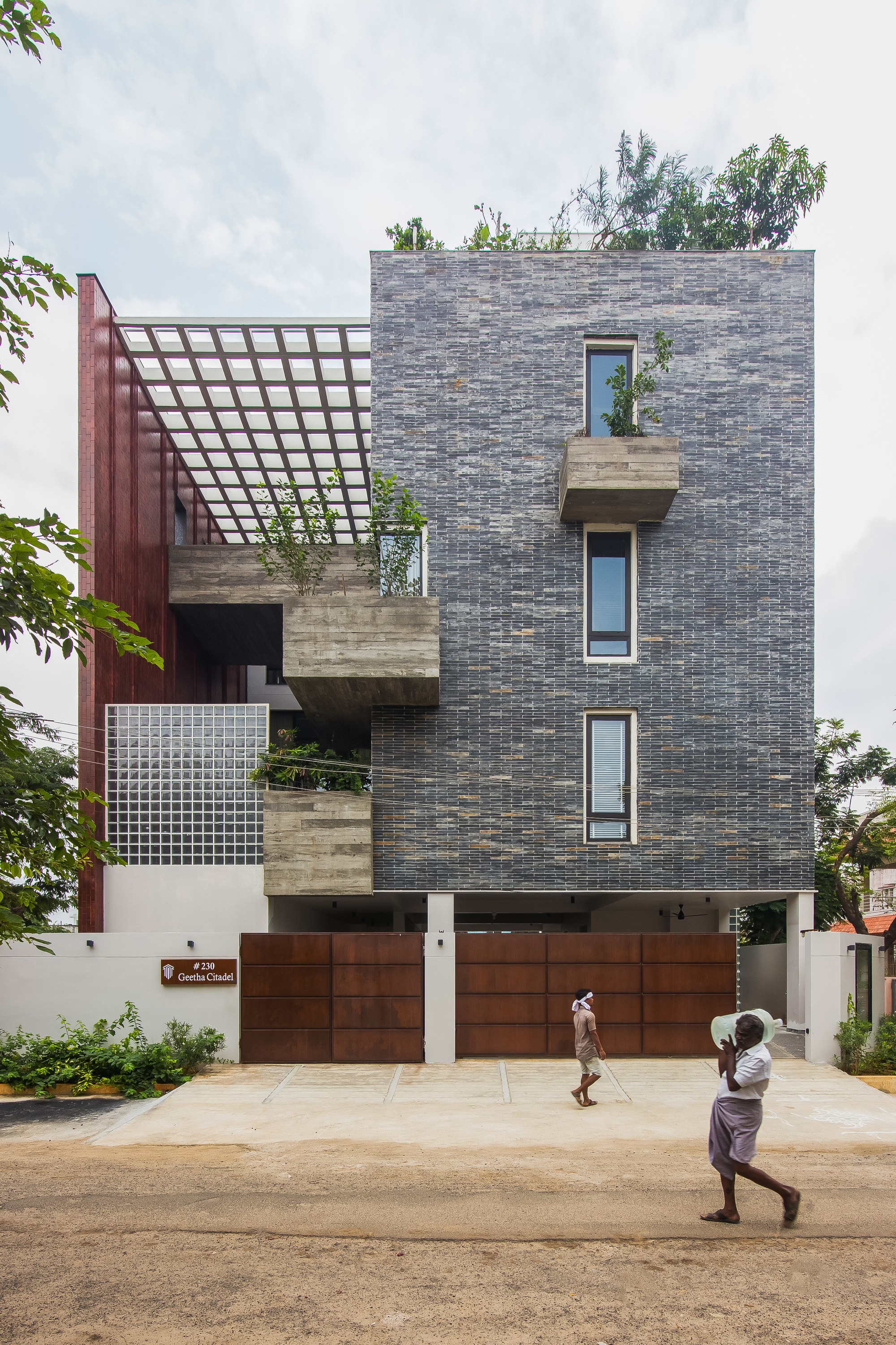 Front elevation showing staggered concrete balconies and timber grid pergola with two pedestrians passing