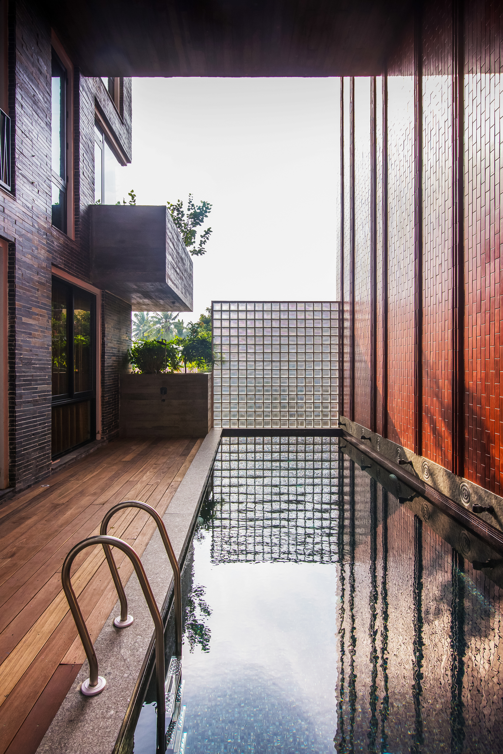Narrow courtyard pool with timber deck and glass block wall under an open sky