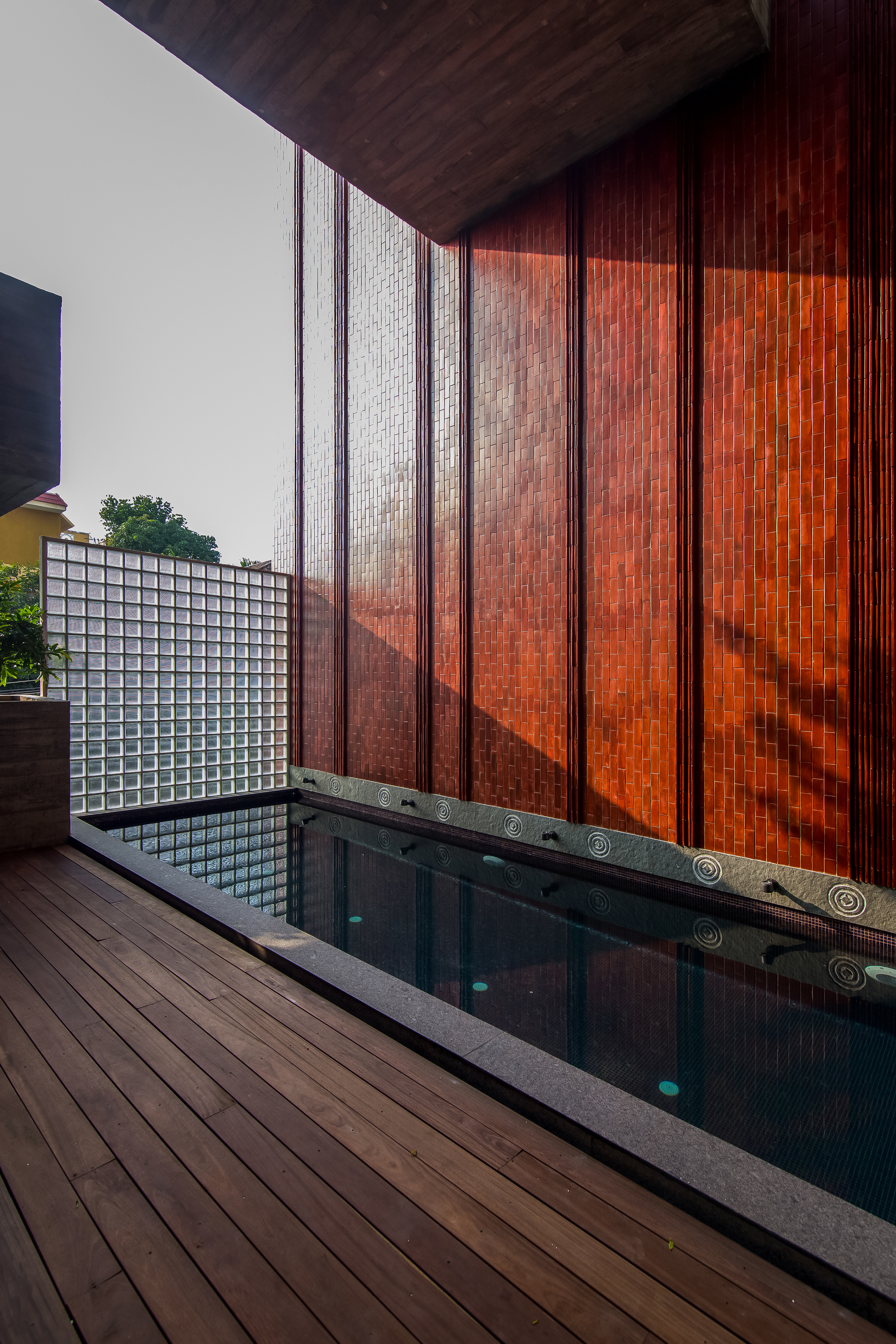 Terrace pool edged with timber decking adjacent to terracotta tile wall and glass block screen