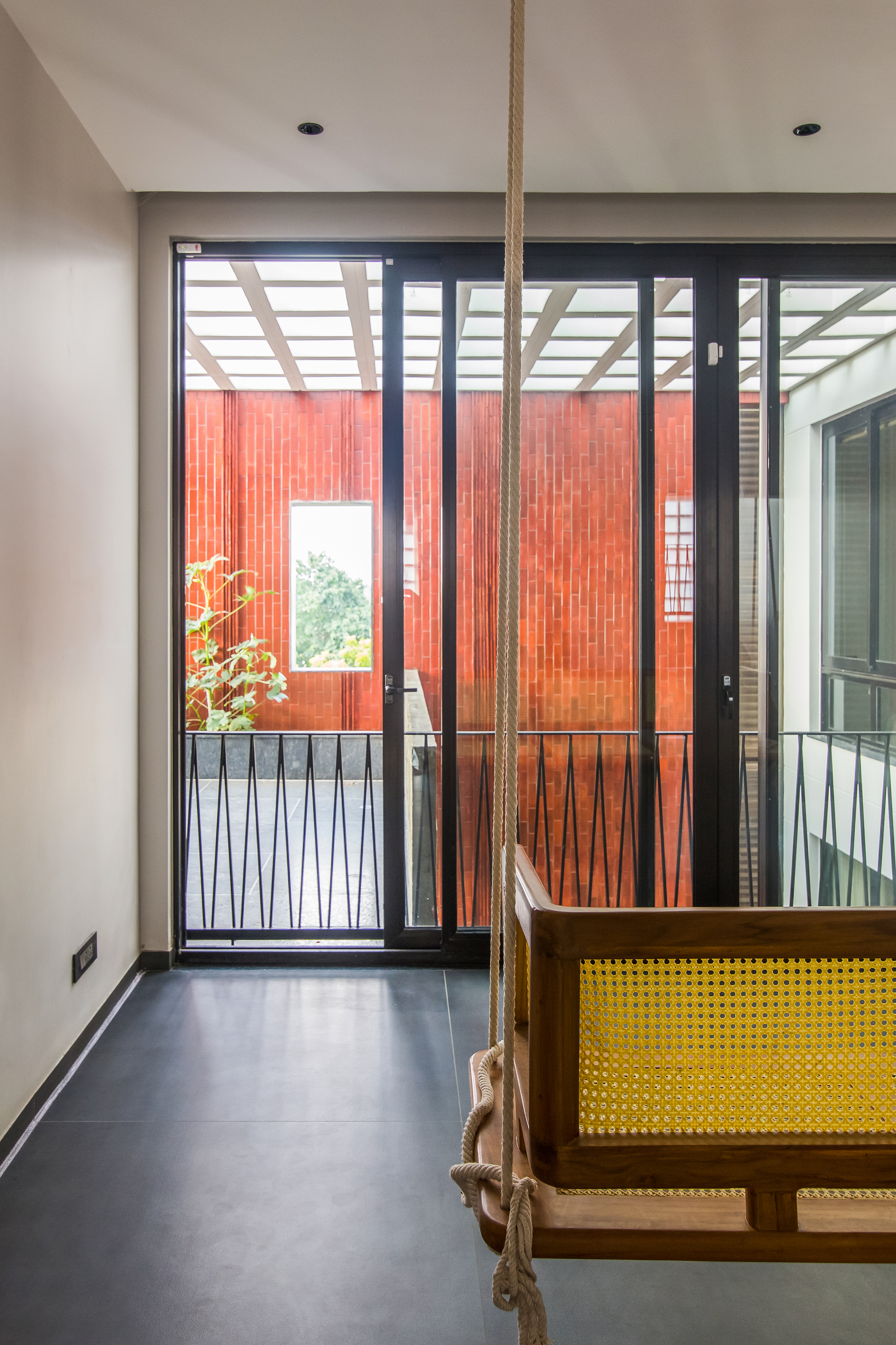 Interior corridor with rope swing and glazed doors opening to terracotta-clad courtyard under pergola