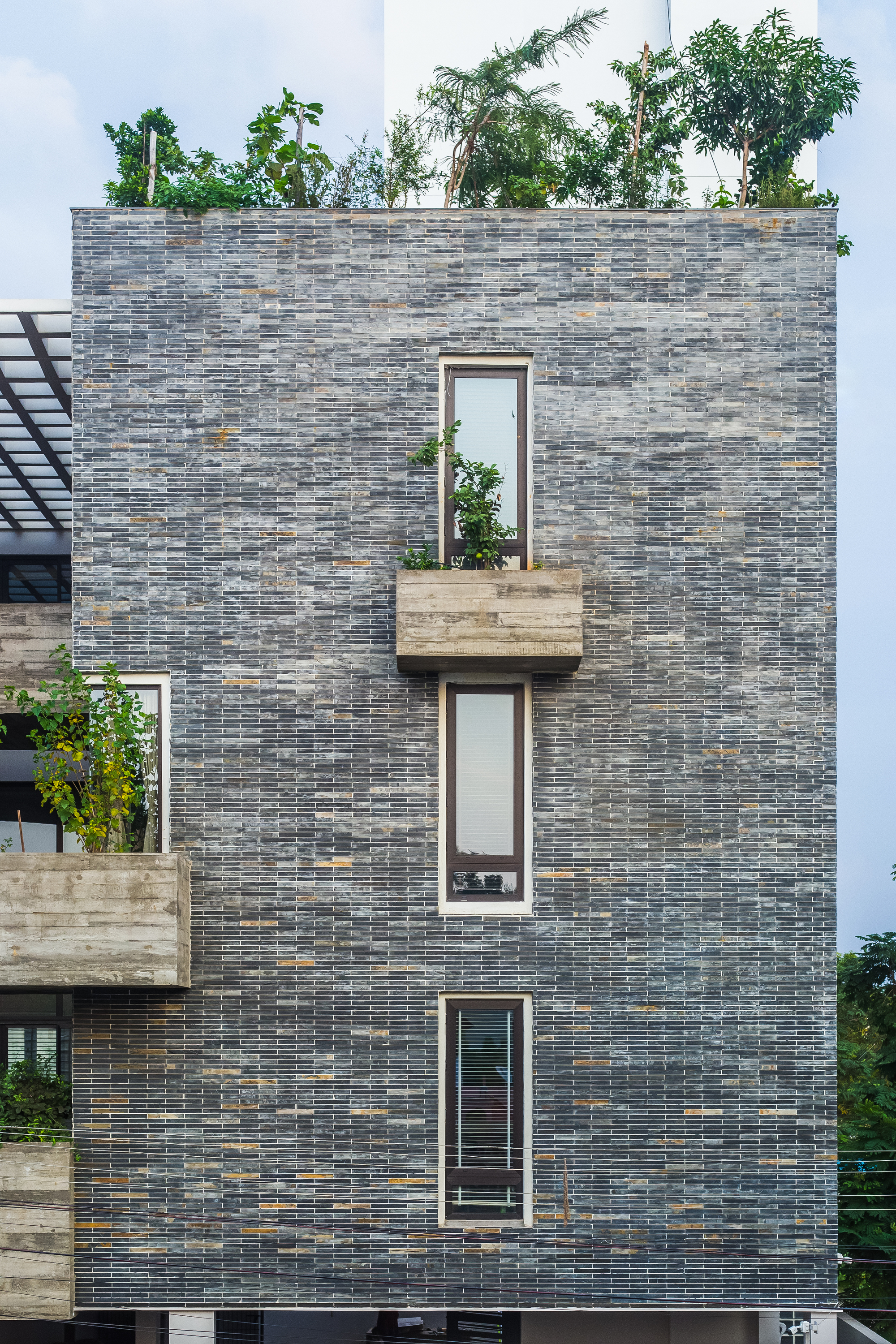 Street facade in variegated grey brick with three cantilevered concrete planters and rooftop greenery