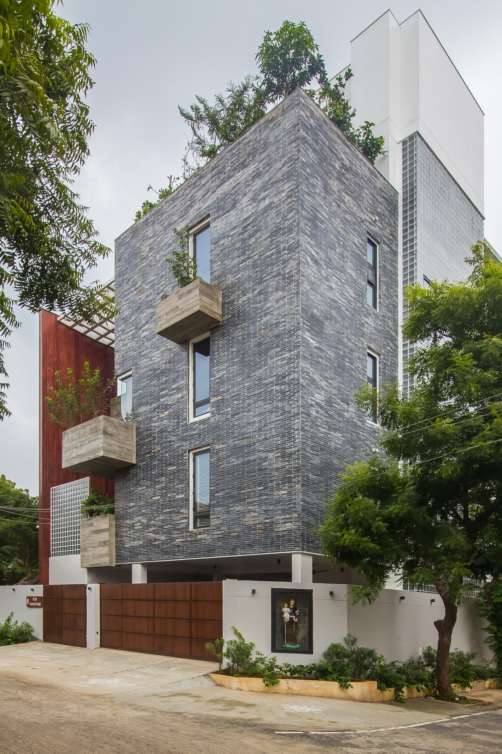 Corner view of the grey brick tower with projecting balconies and surrounding trees under overcast sky