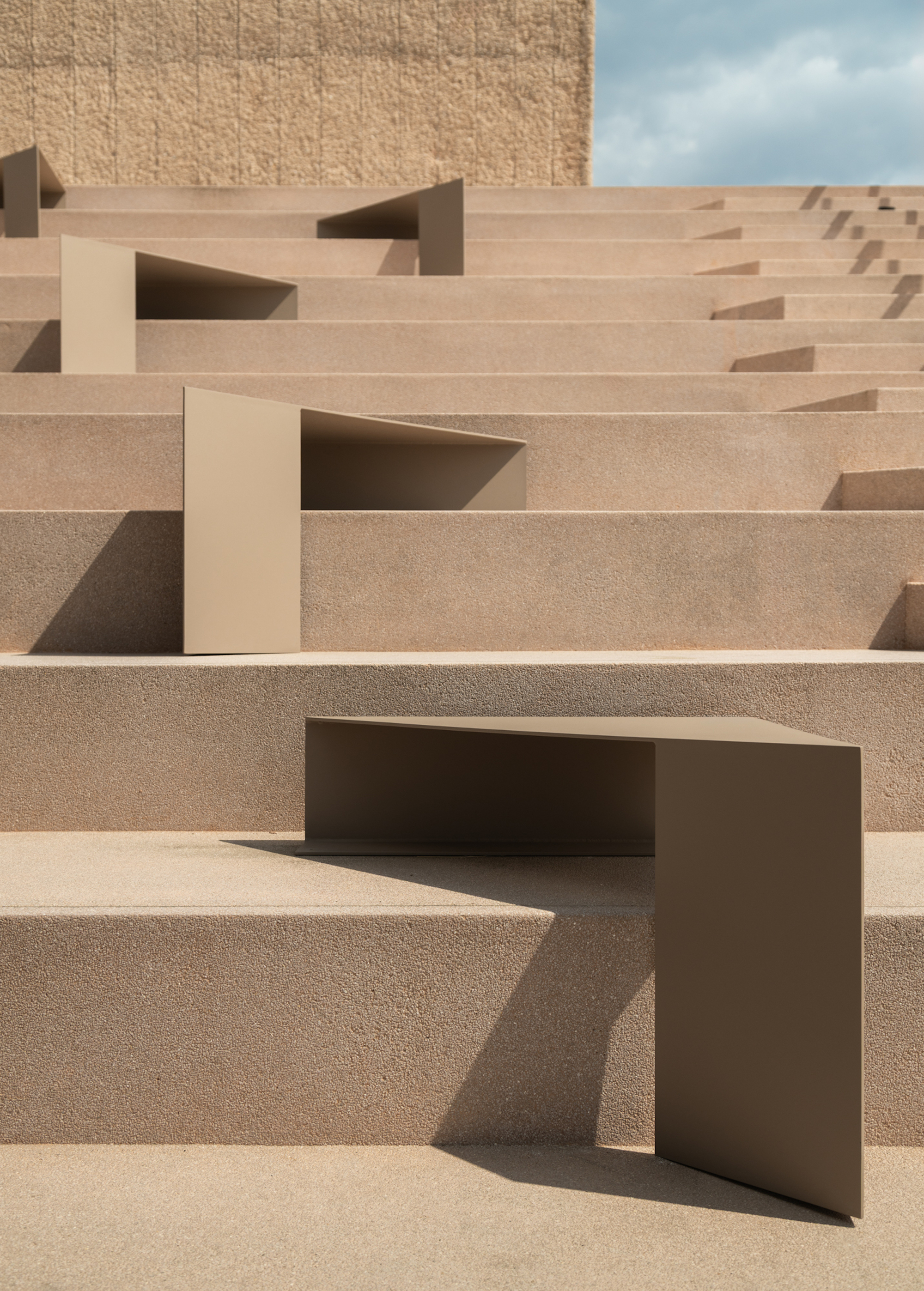 Textured aggregate stair treads with folded metal sheet seating elements under bright sunlight