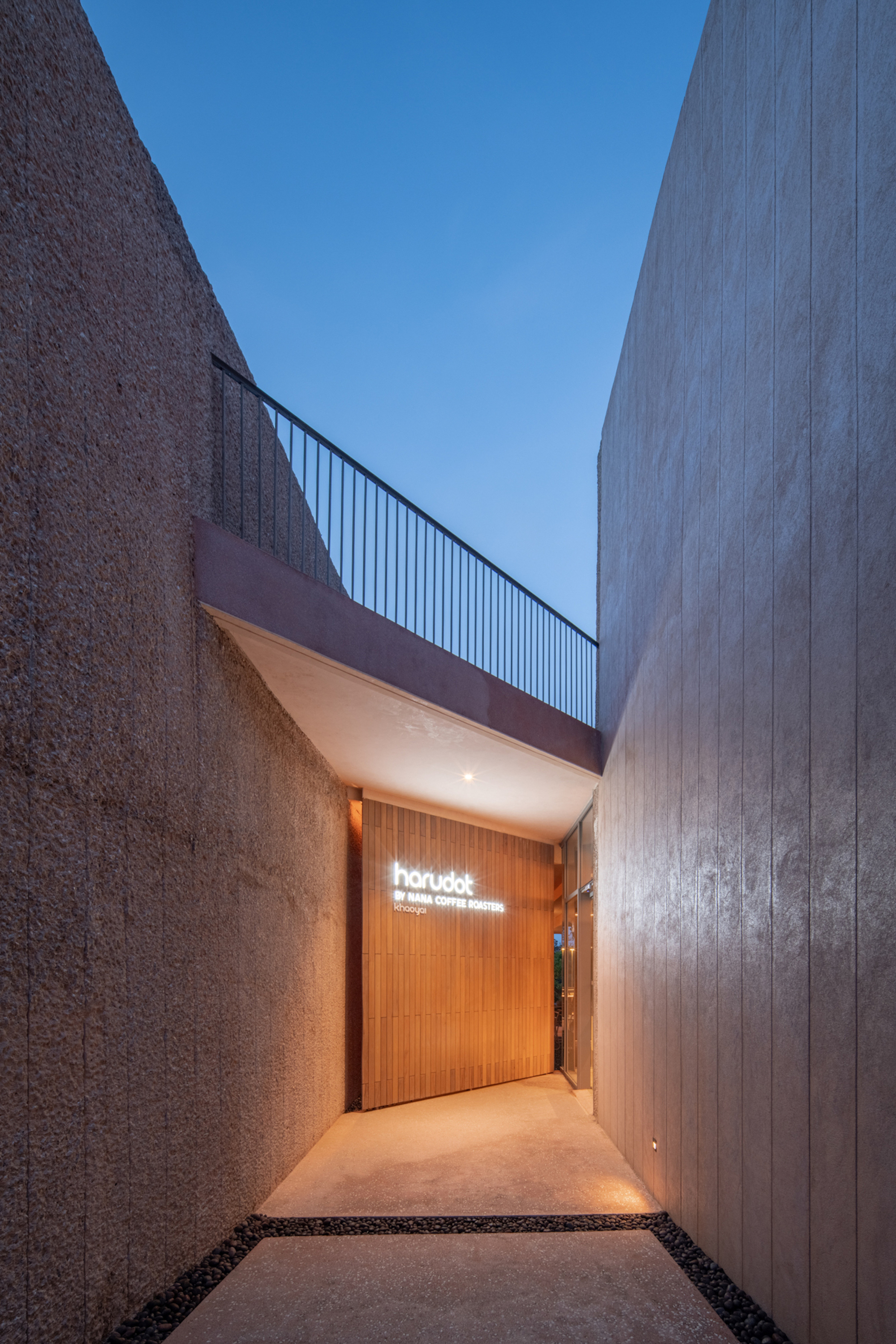 Narrow entry passage between textured concrete walls leading to timber door with illuminated signage