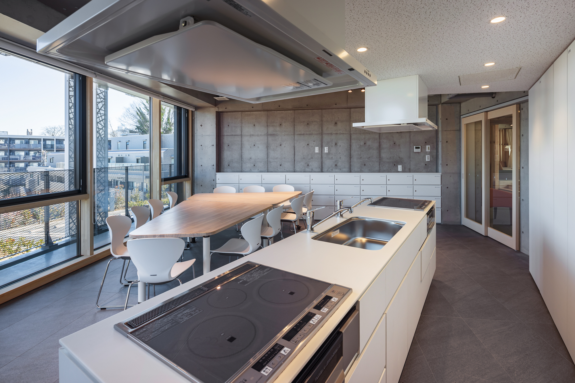 Shared kitchen with white island, integrated cooktop and concrete wall behind a dining table near corner windows