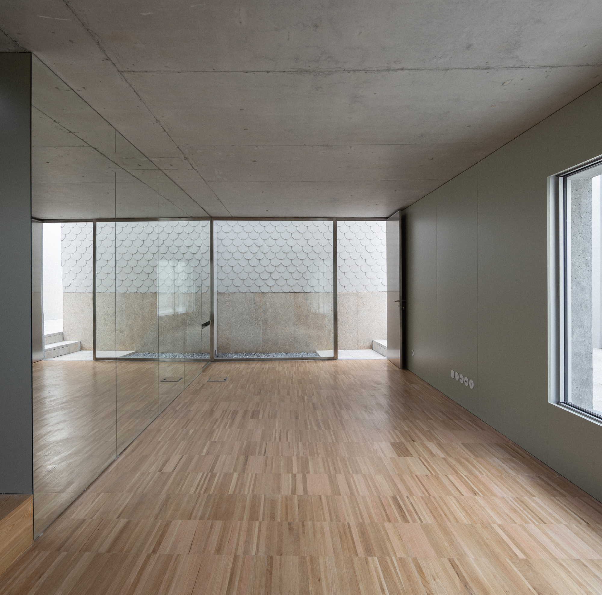 Interior room with wood flooring and concrete ceiling overlooking a courtyard through full-height glazing