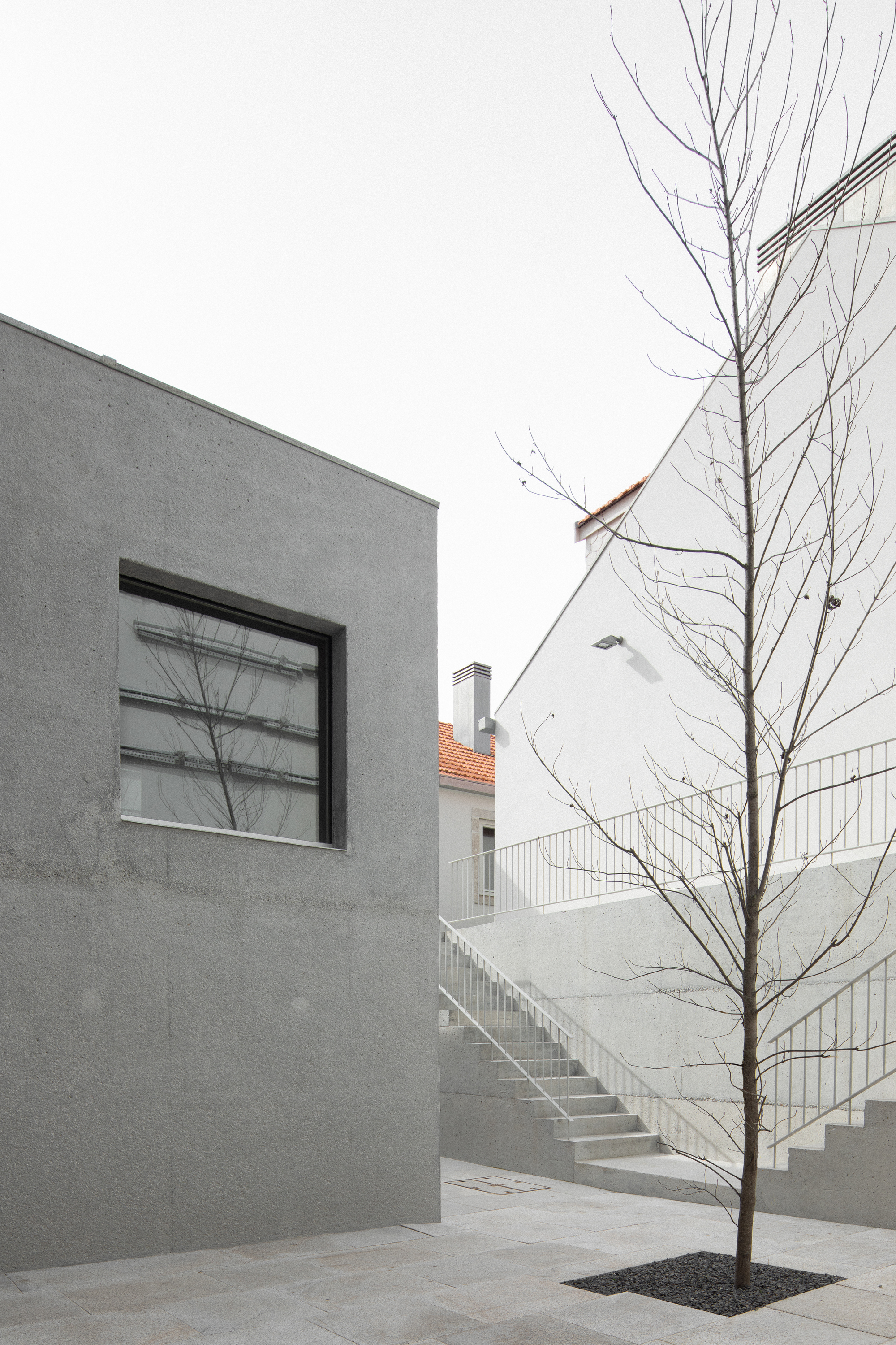 Courtyard view showing a grey rendered wall with square window and bare tree beside an exterior staircase