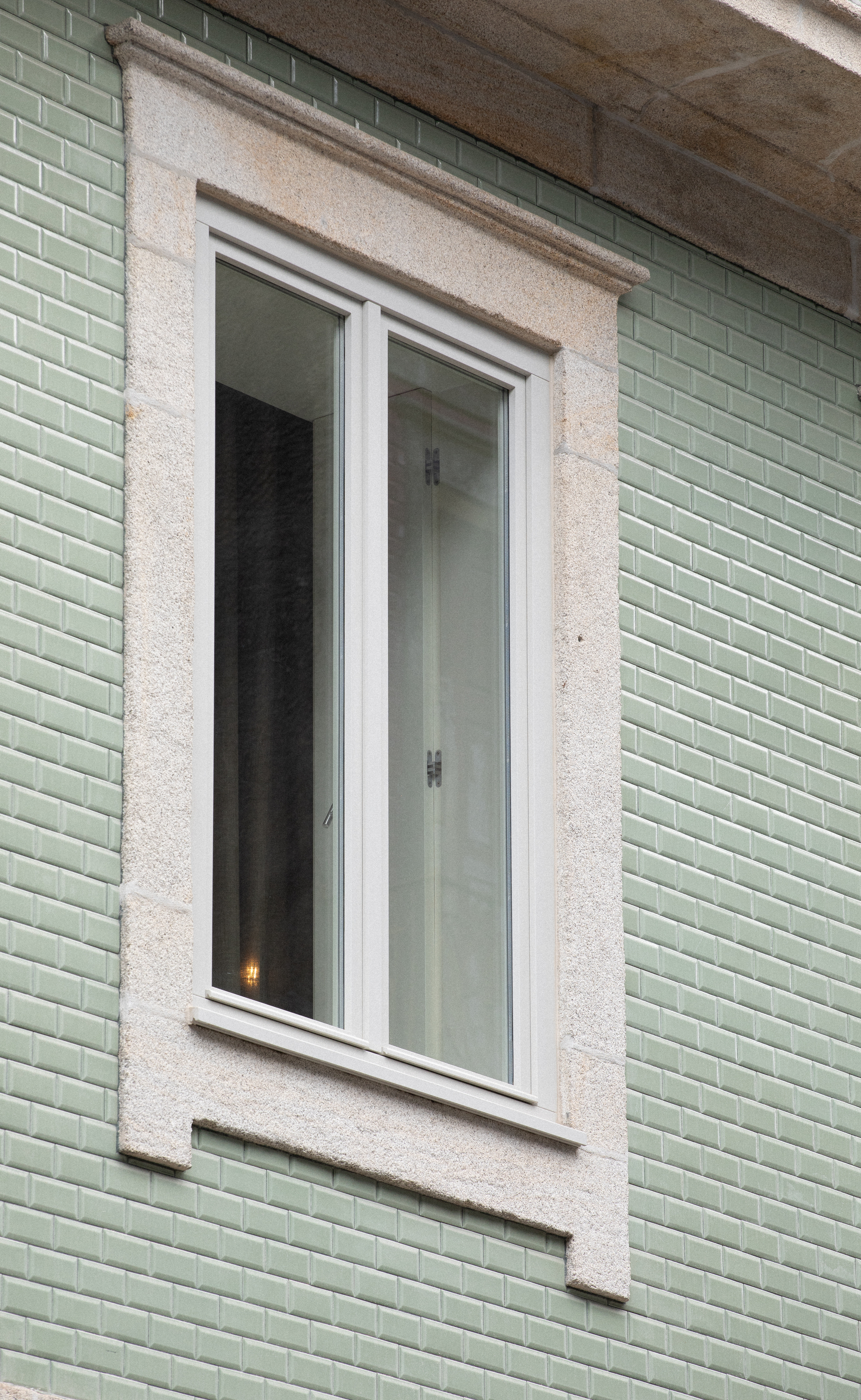 Detail of a white casement window framed in terrazzo surround against pale green glazed tile cladding