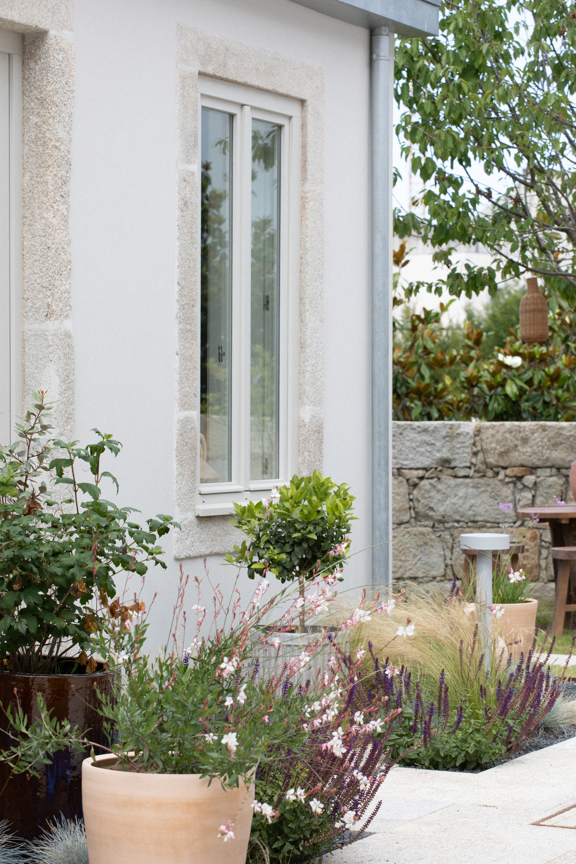 Narrow glazed window with stone surround beside terracotta pots and flowering plants