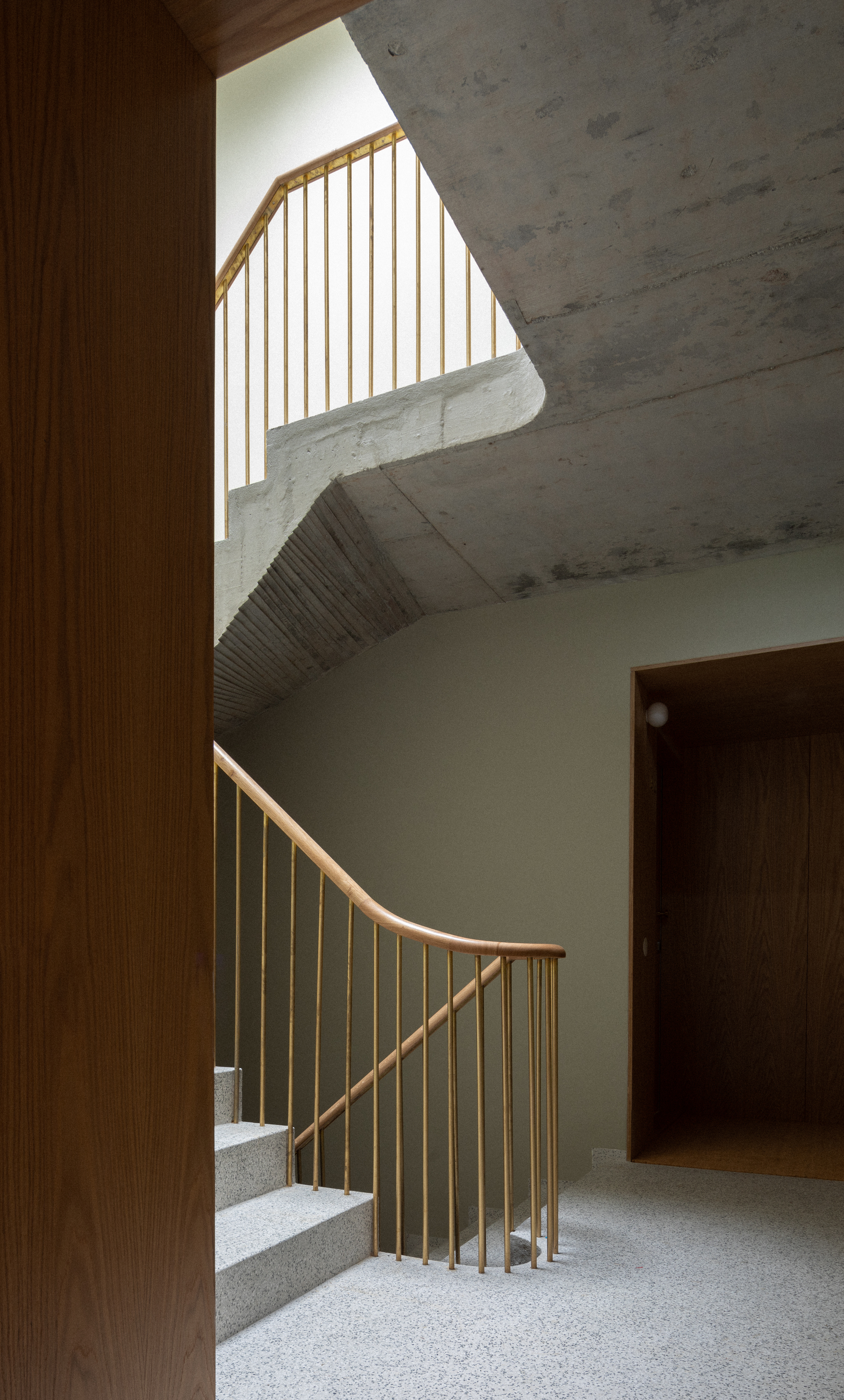 Timber-railed staircase with terrazzo treads framed by exposed concrete ceiling and wood-paneled walls