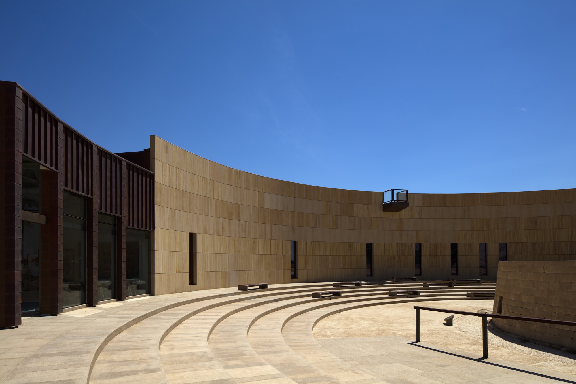 Curved outdoor amphitheater with concentric stone seating tiers under a clear blue sky