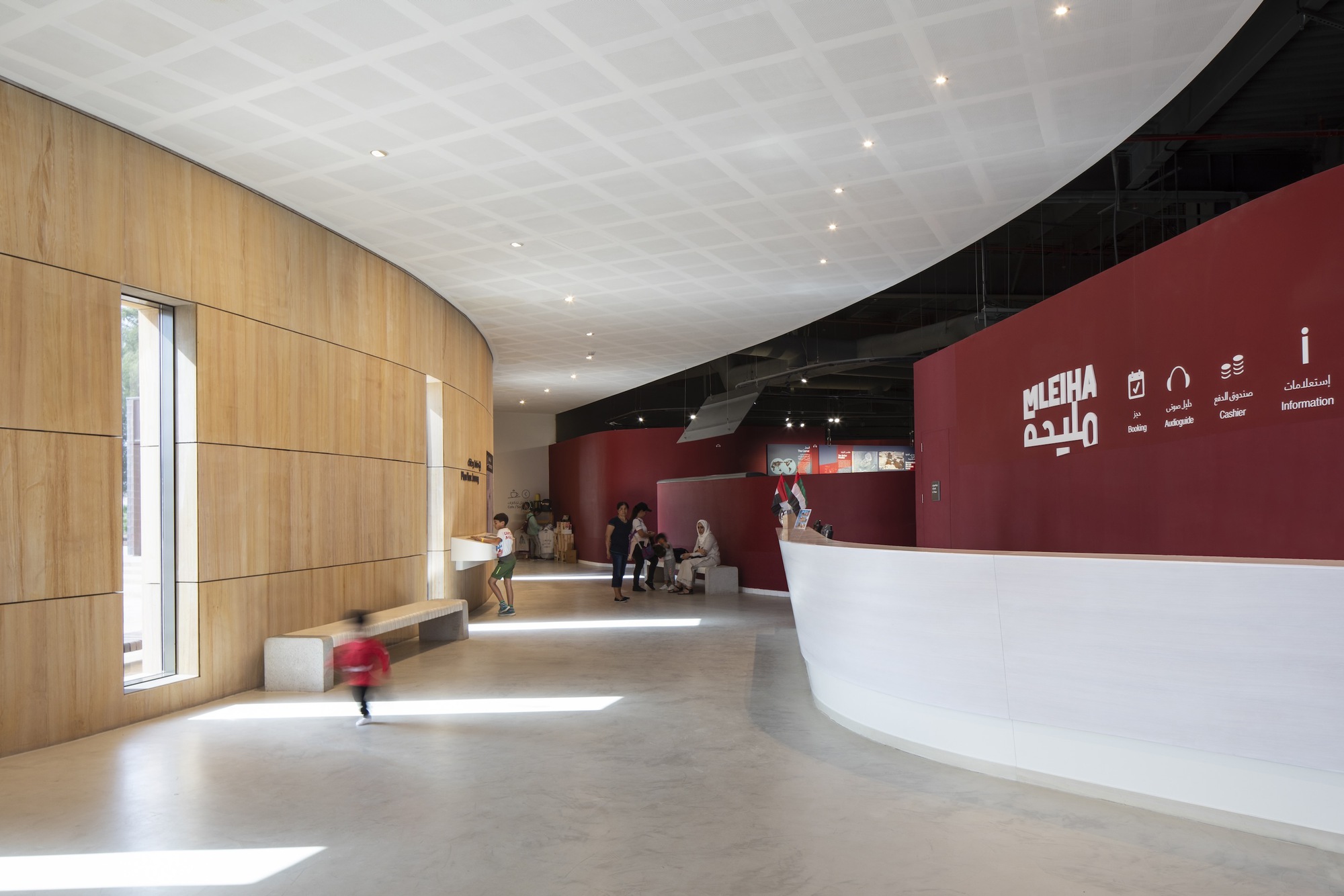Reception lobby with curved timber wall, white coffered ceiling, and visitors at seating area