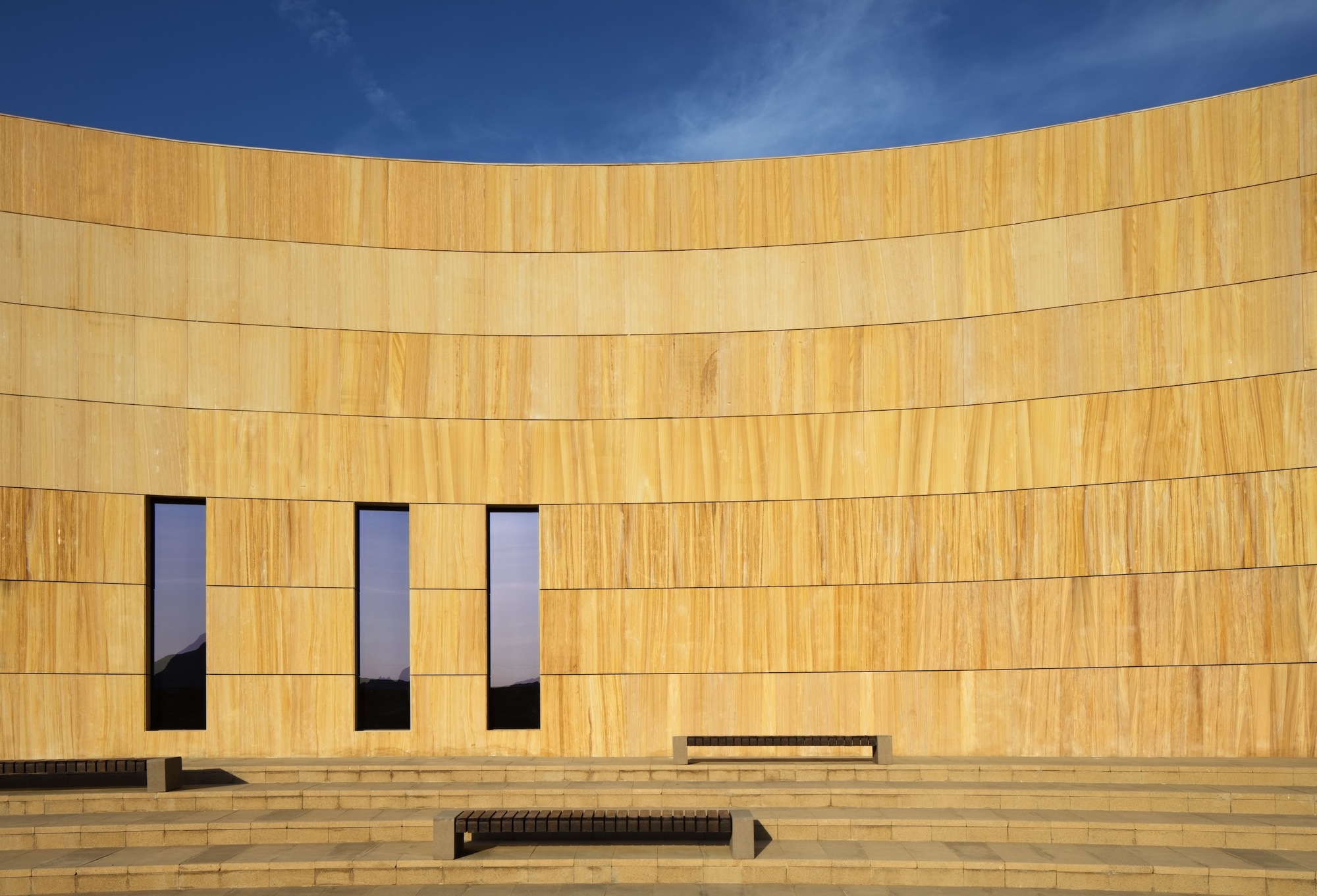 Close view of the curved sandstone facade with three tall narrow windows and stepped terrace below