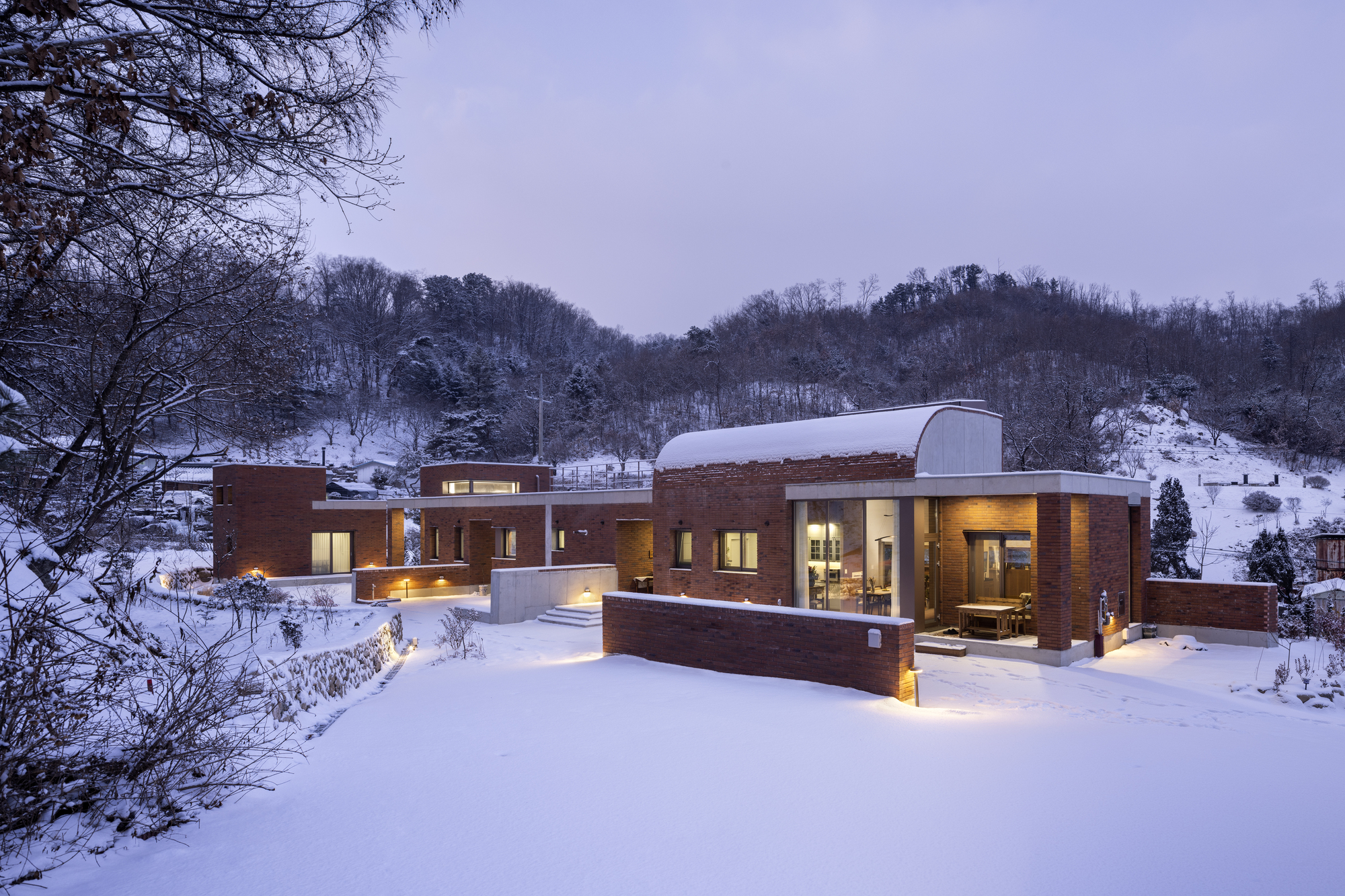 Brick residence with barrel vaulted roof set in a snow-covered hillside landscape at dusk