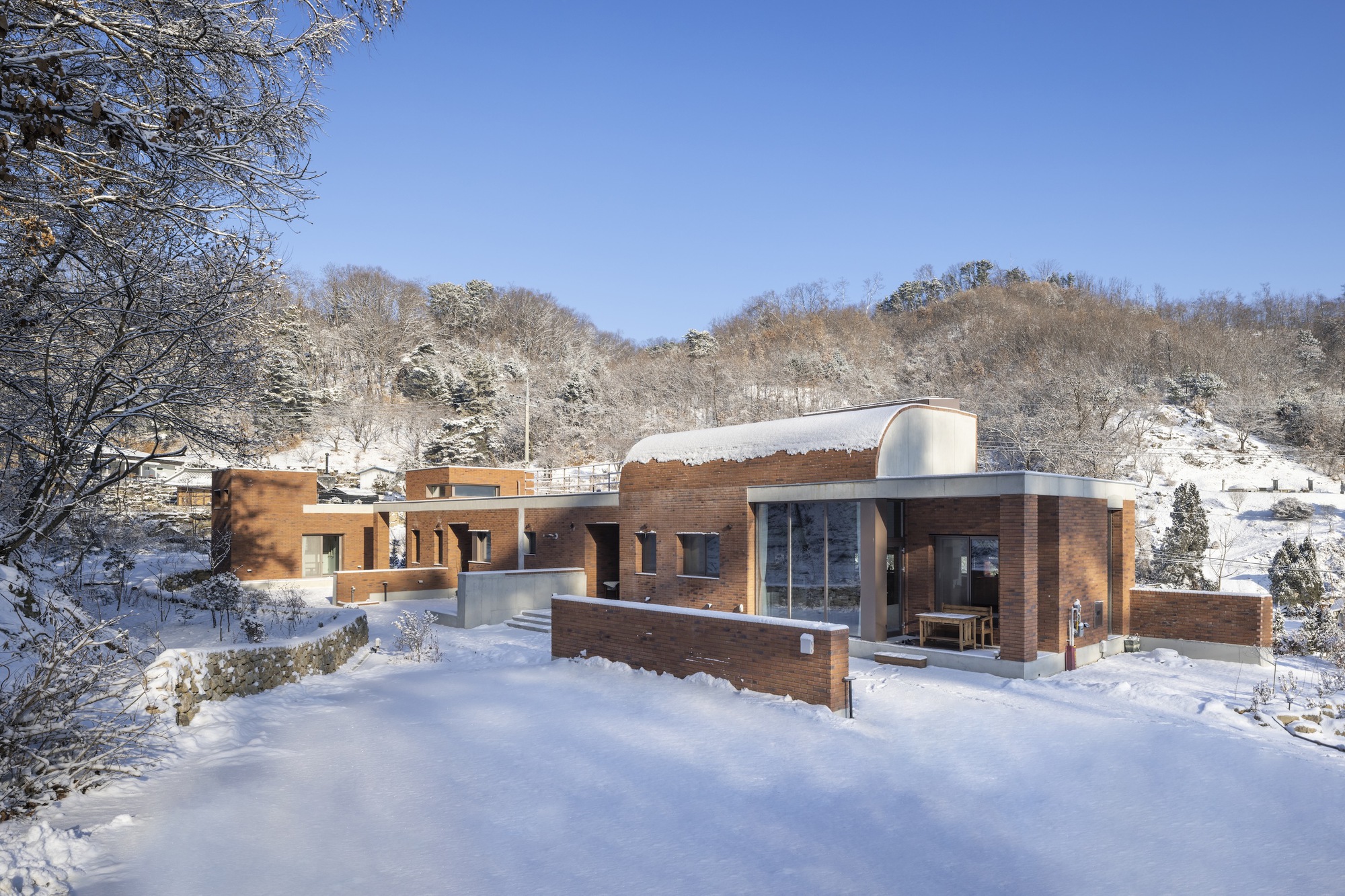 Horizontal brick volumes with curved roof element nestled in a winter valley beneath clear blue sky