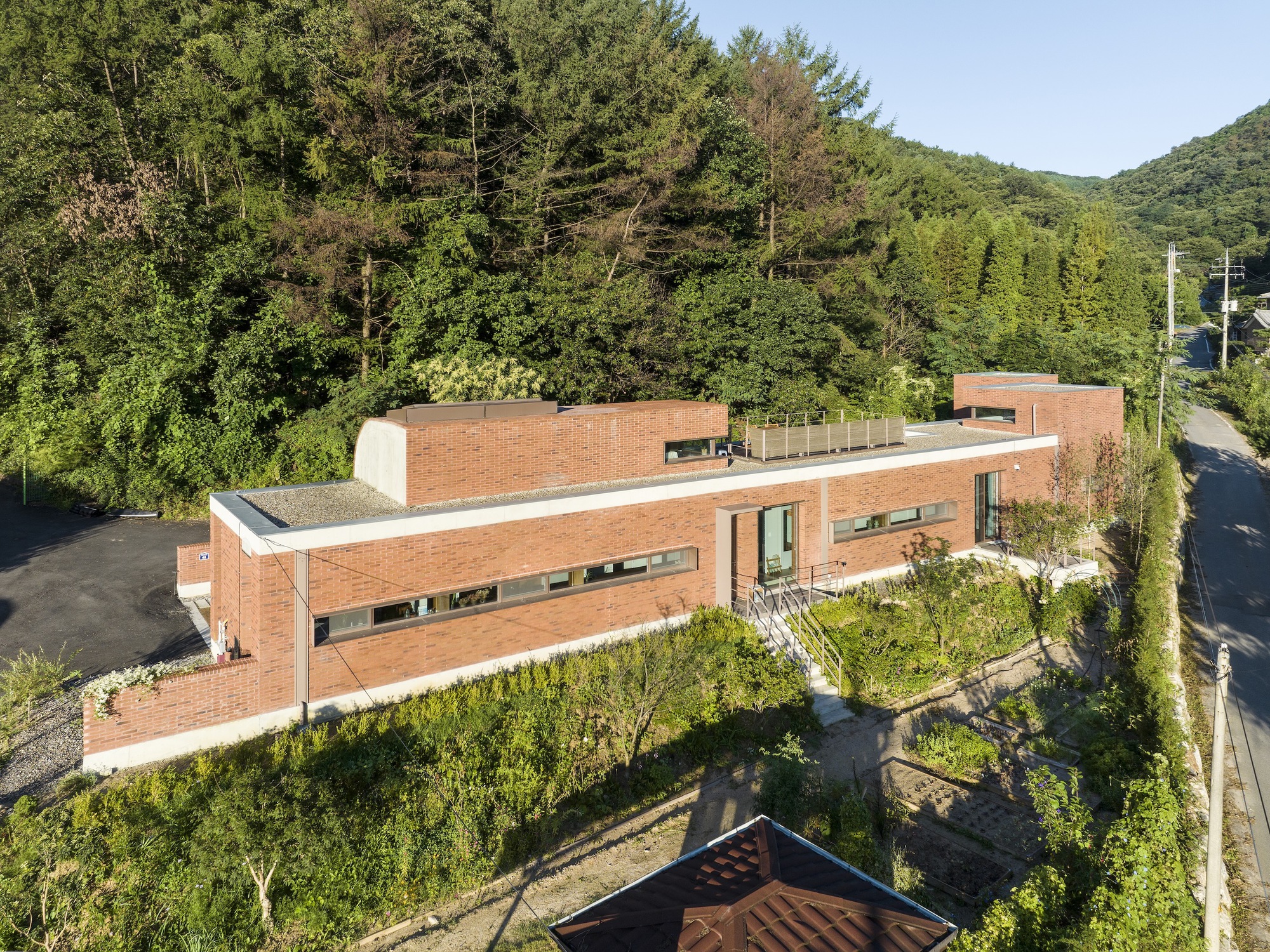 Aerial view of the stacked brick volumes and rooftop terrace surrounded by dense summer foliage