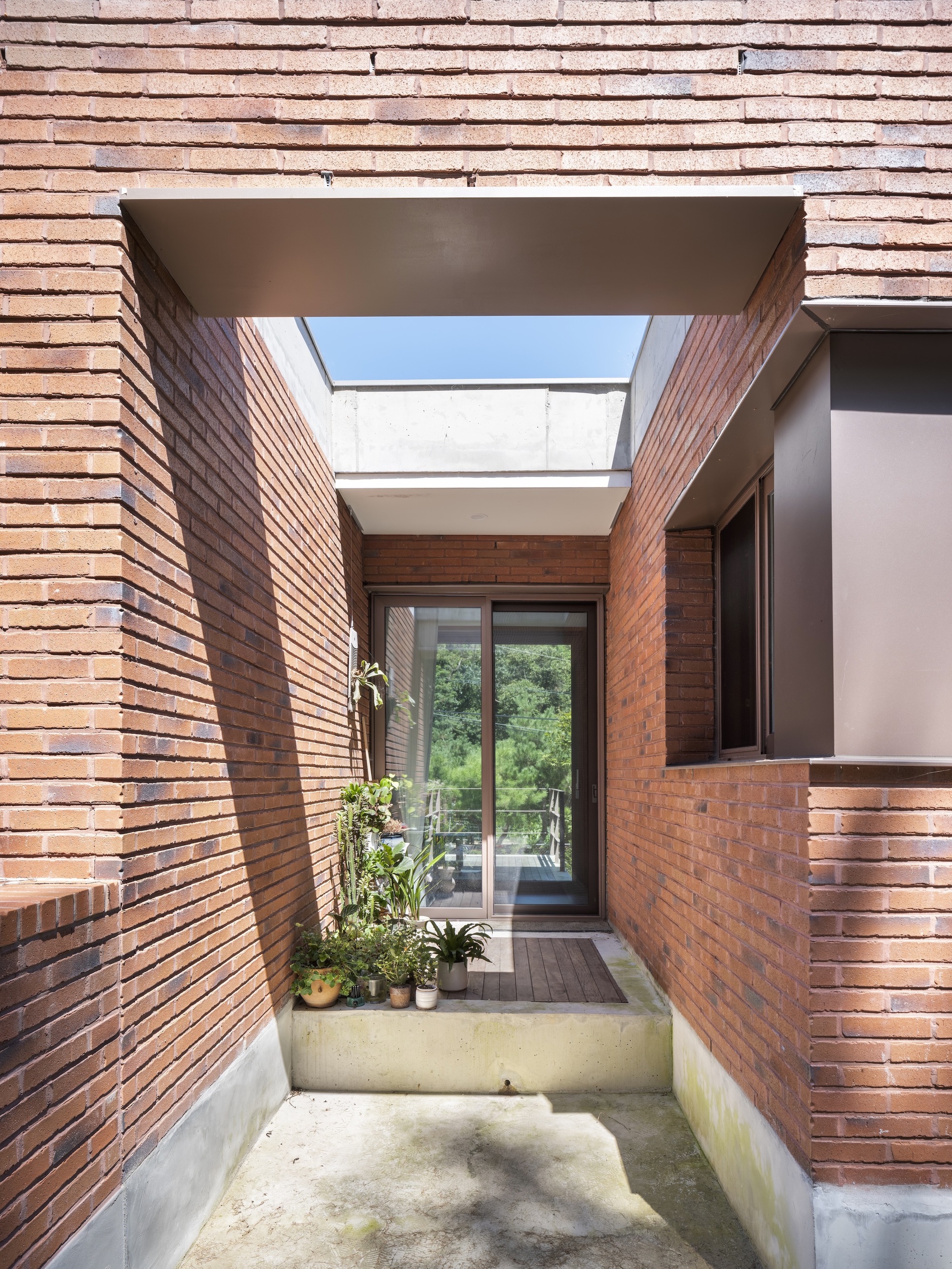 Brick-lined entry court with skylight overhead and potted plants along the concrete base