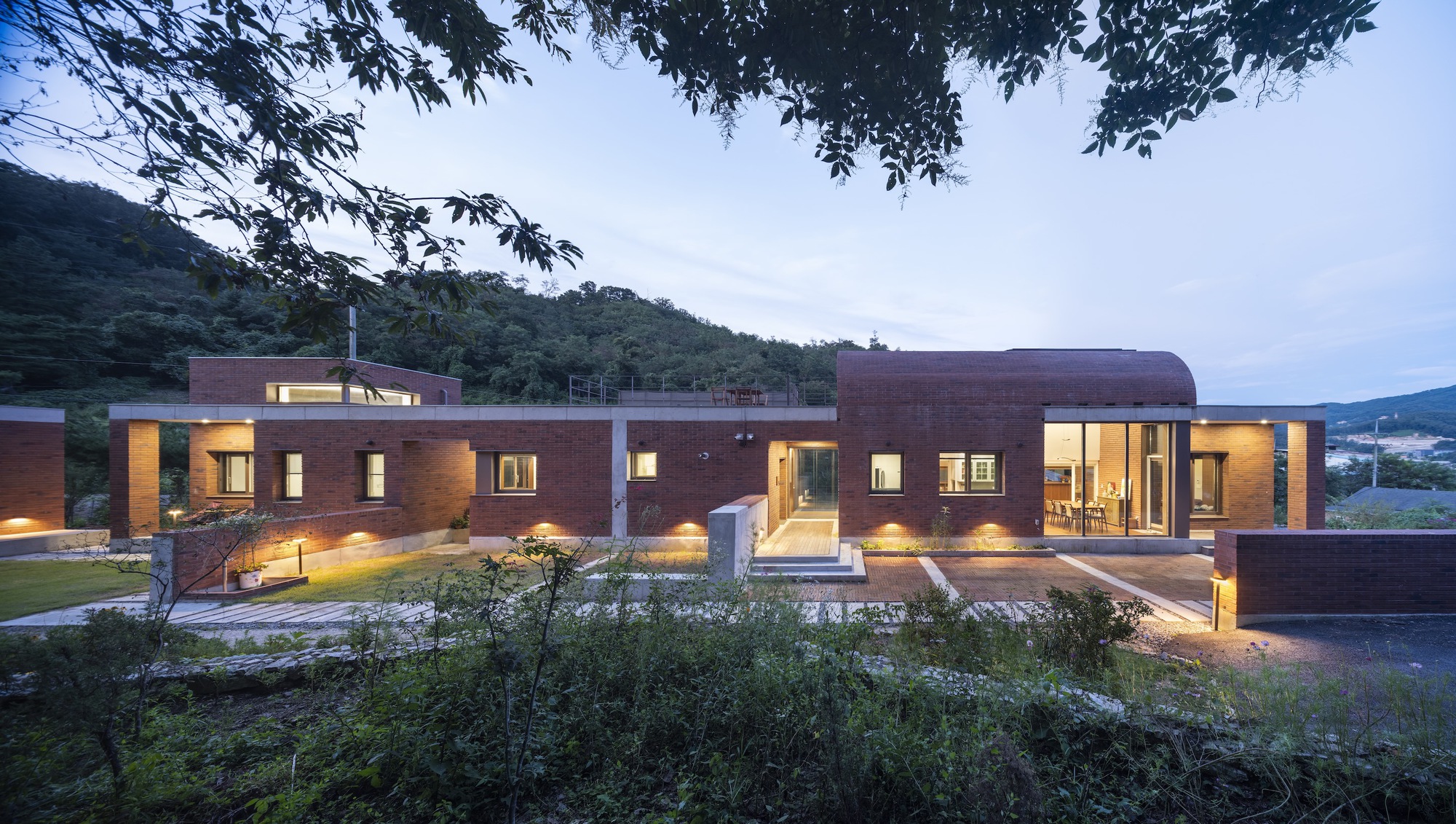 Evening view of the brick facade with illuminated windows and landscaped foreground planting beds