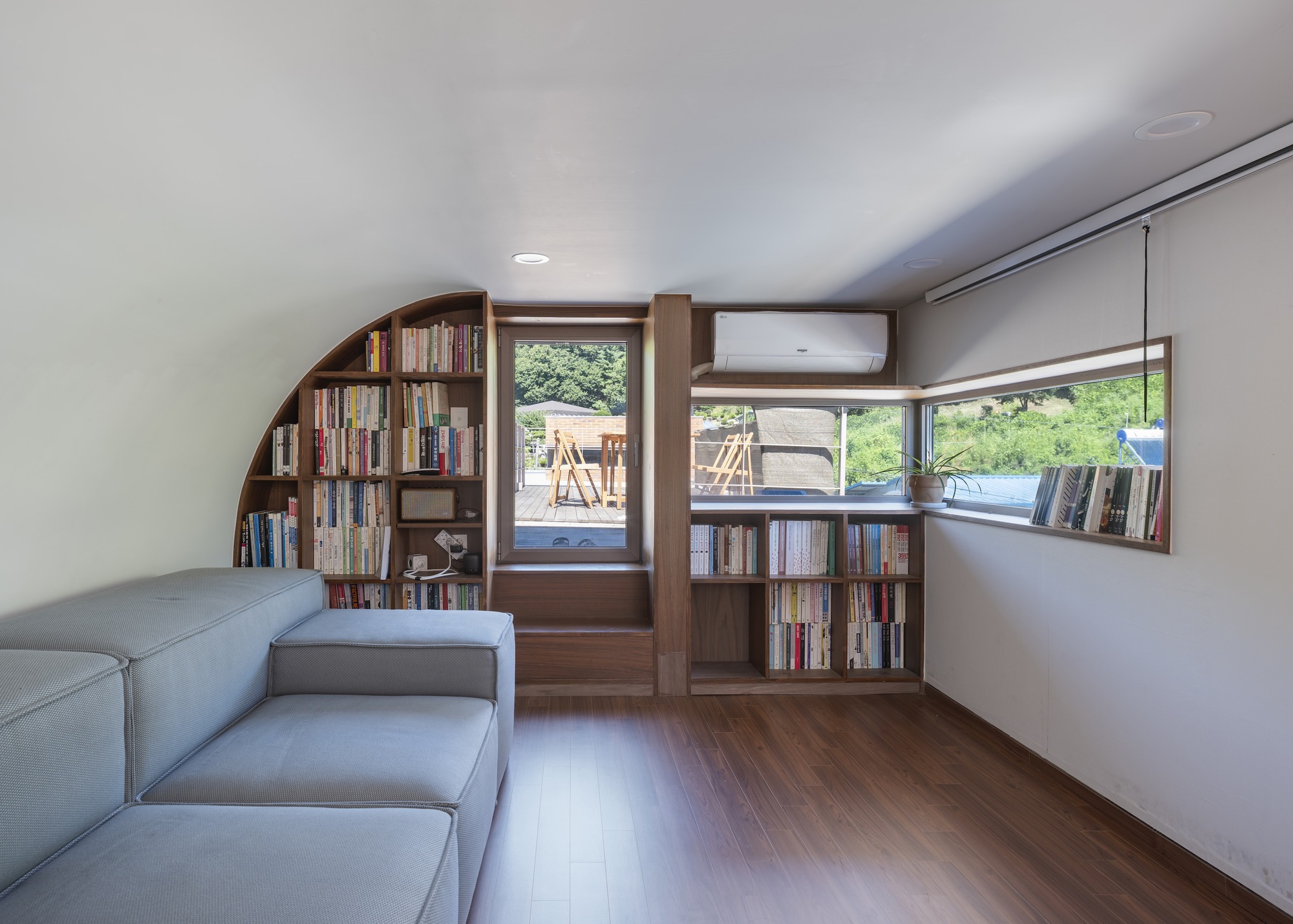 Reading room with curved timber bookshelves and corner windows overlooking the surrounding greenery