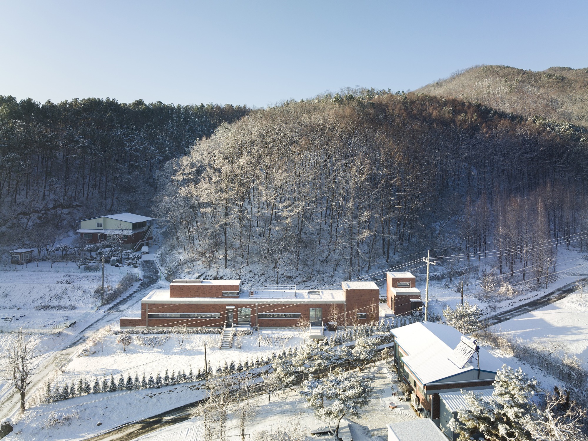 Aerial view of the horizontal brick volumes set into a snowy hillside with frosted trees behind