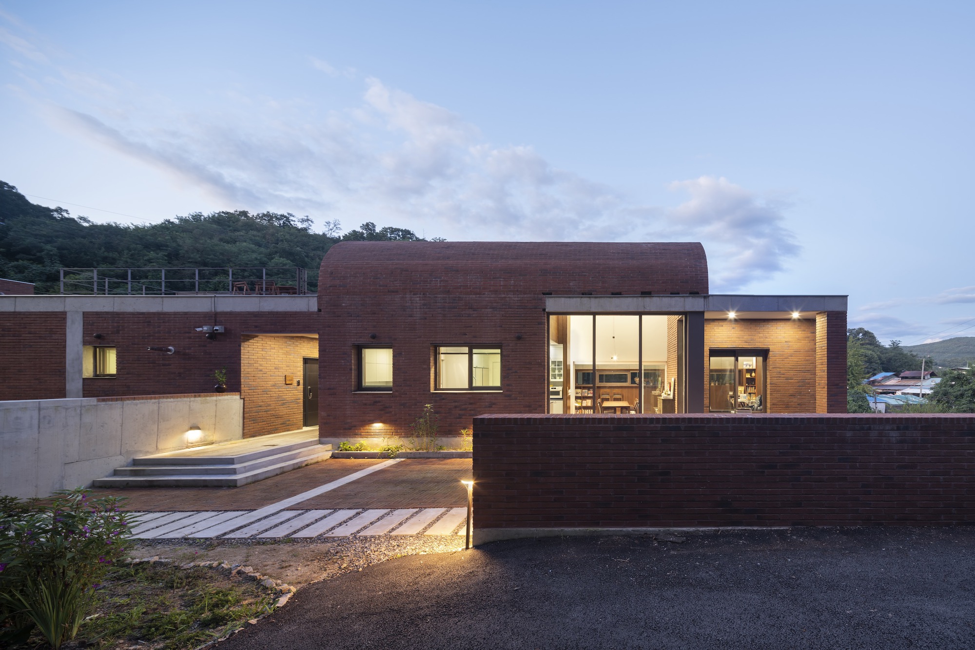 Dark brick facade with illuminated glazing and timber walkway at dusk