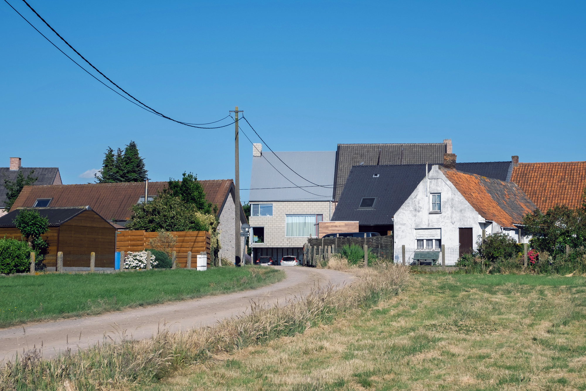 Street view showing the pale brick volume inserted between traditional pitched-roof houses under a clear sky