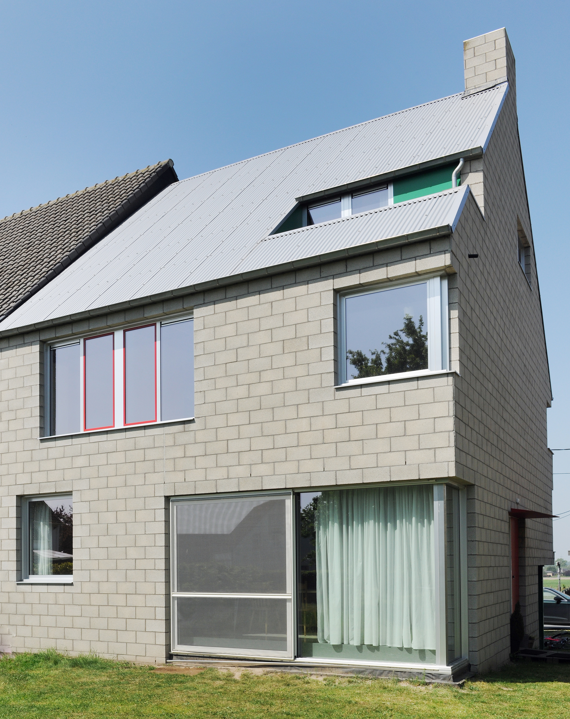 Side facade displaying pale masonry walls, corrugated roof slope, and stacked window openings with green accents